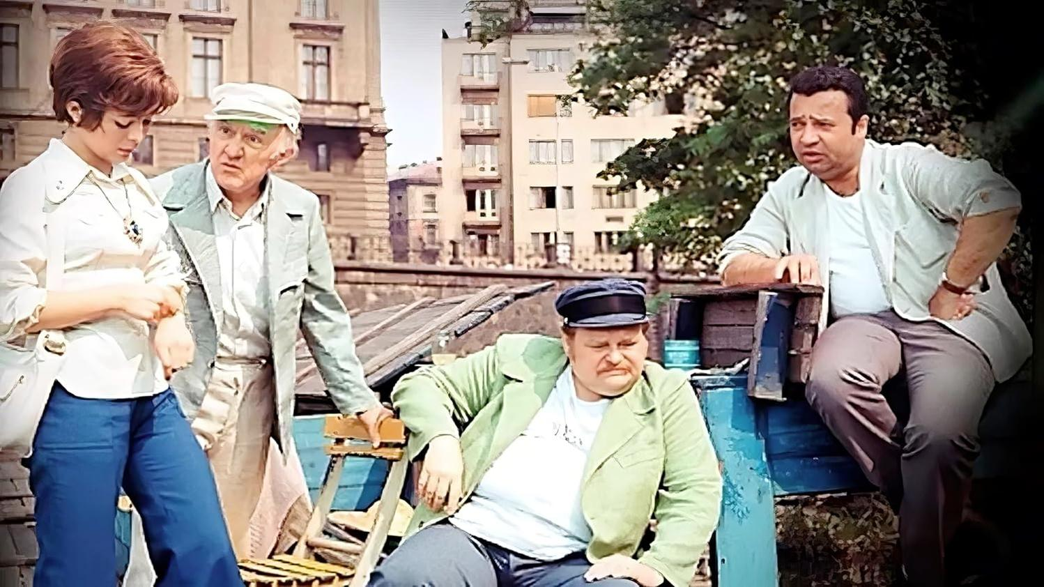 Vier Personen in Vintage-Kleidung im Freien, Gebäude und Bäume im Hintergrund.