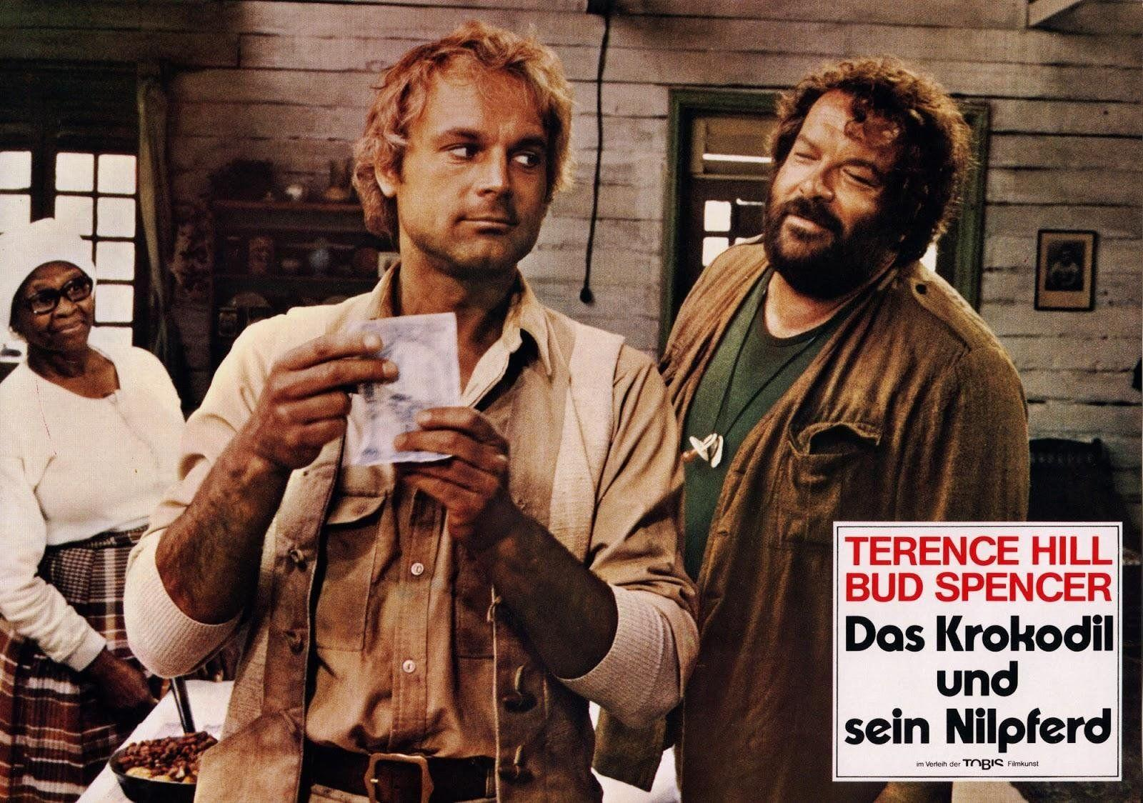 Drei Personen in einem rustikalen Raum. Mann hält Papier. Frau in Weiß, Mann mit Bart.