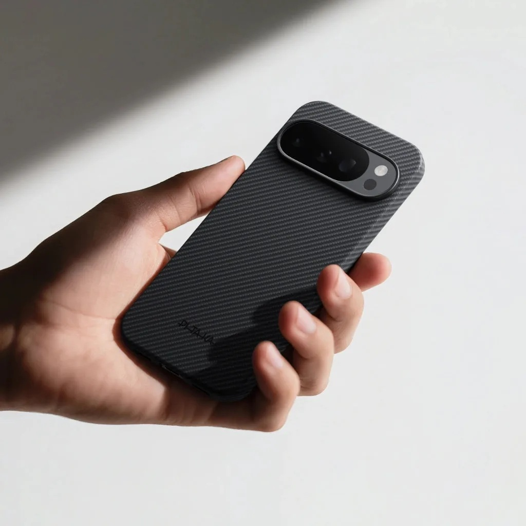 Dłoń trzyma ciemny smartfon w etui z wzorem włókna węglowego. Zestaw aparatów na górze.