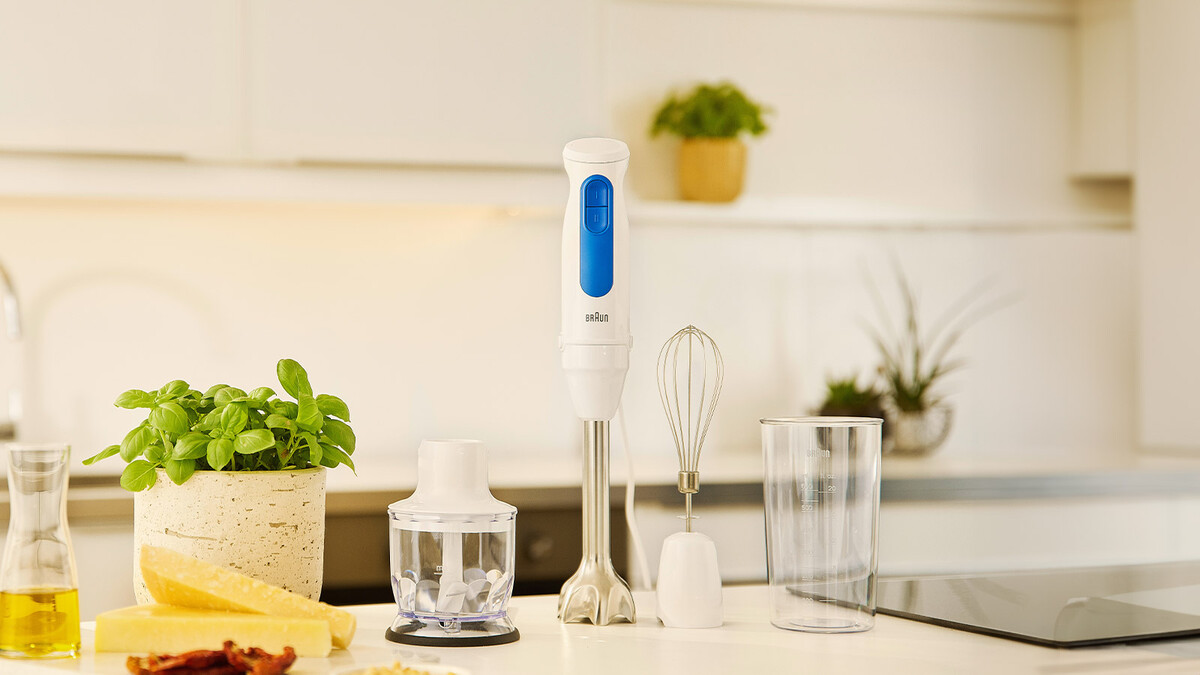 Braun hand blender with accessories on a kitchen counter with basil, cheese, and oil.