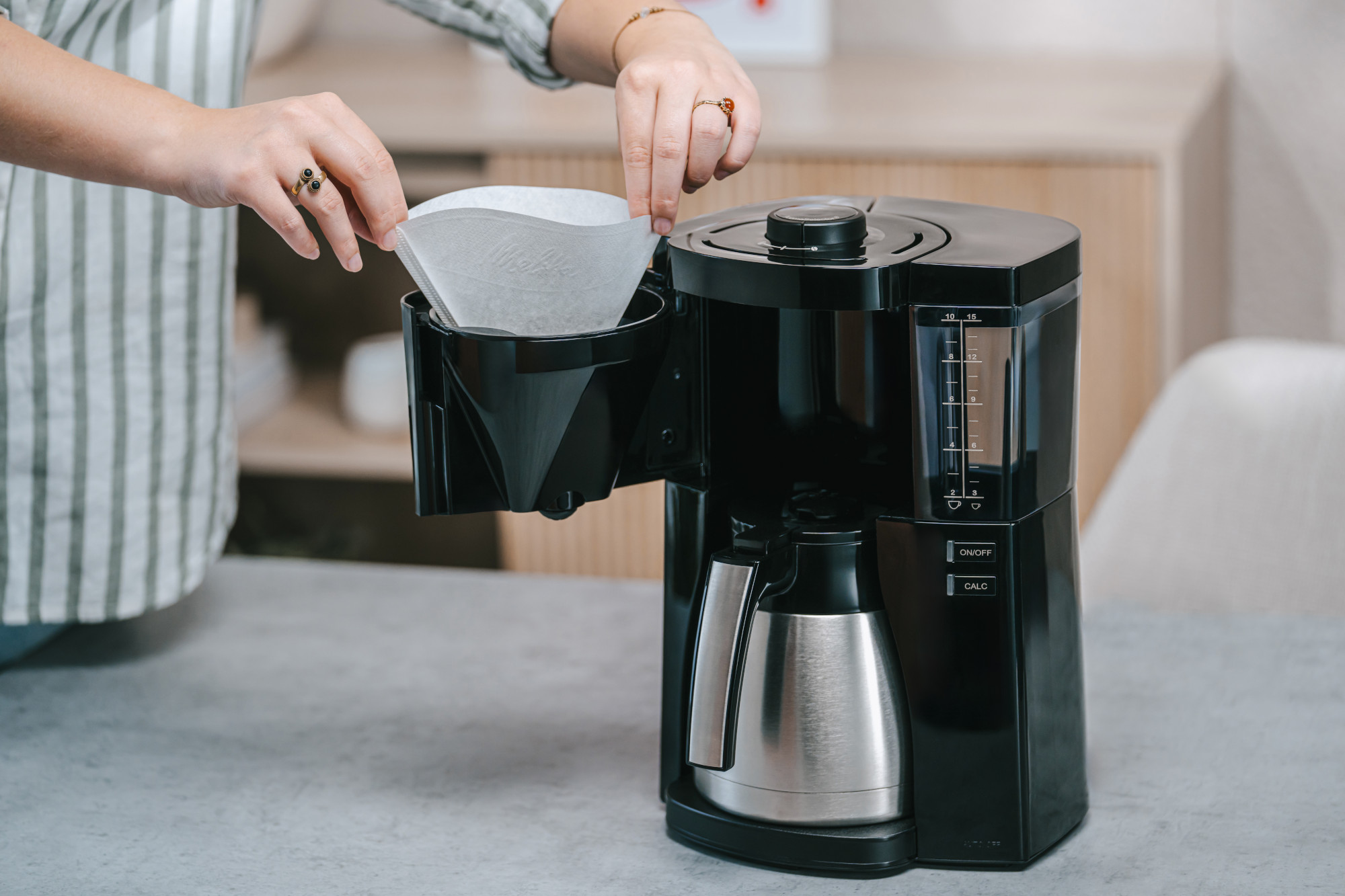 Une personne place un filtre à café dans une cafetière noire avec une carafe argentée.