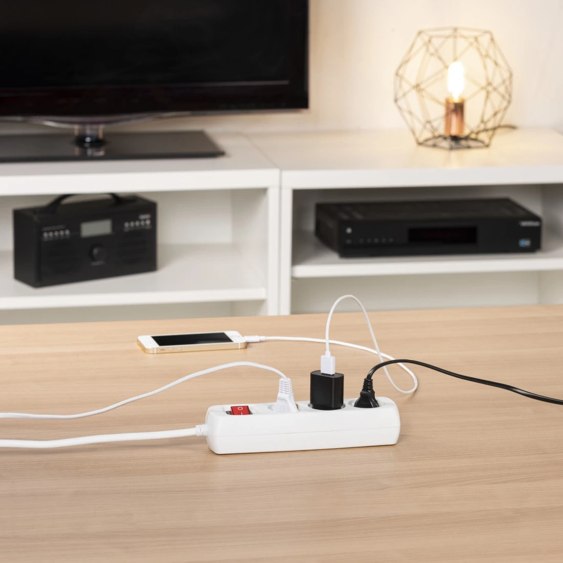 Una regleta con interruptor rojo carga un teléfono, con cables conectados a cargadores.