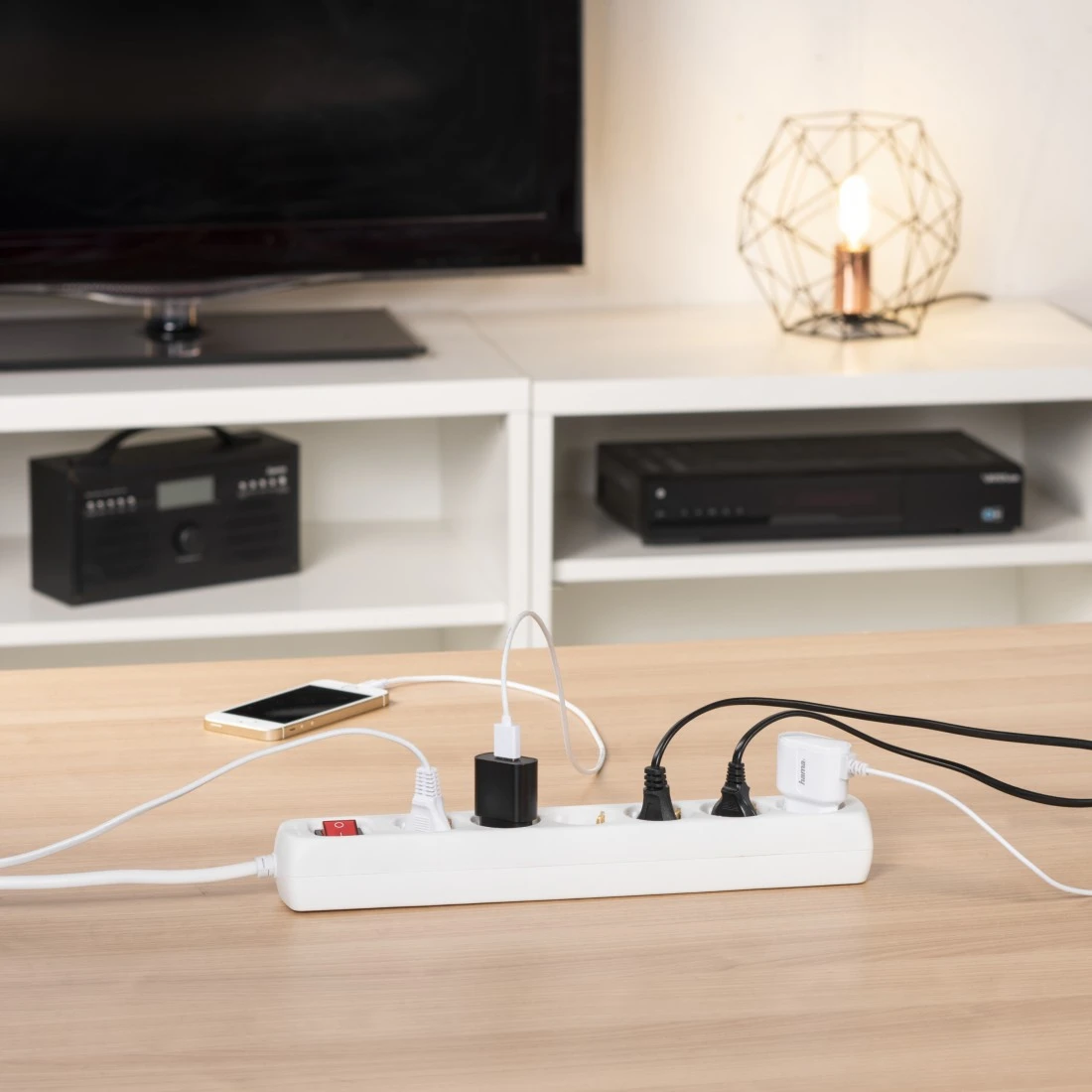 Una regleta con varios enchufes y un teléfono cargando sobre una mesa de madera.