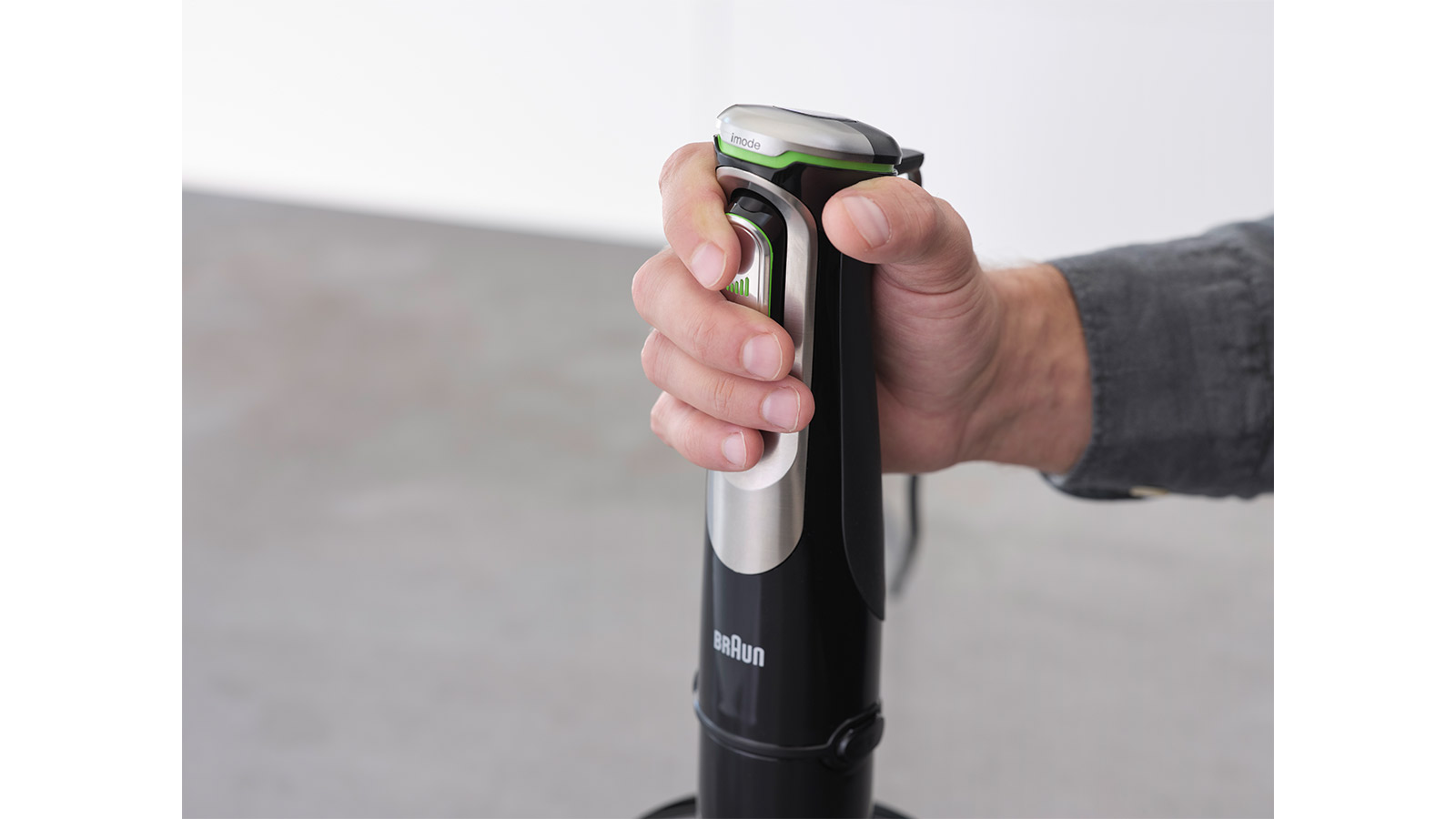 Hand hält schwarzen Stabmixer mit silbernen Details und grüner Akzentbeleuchtung.