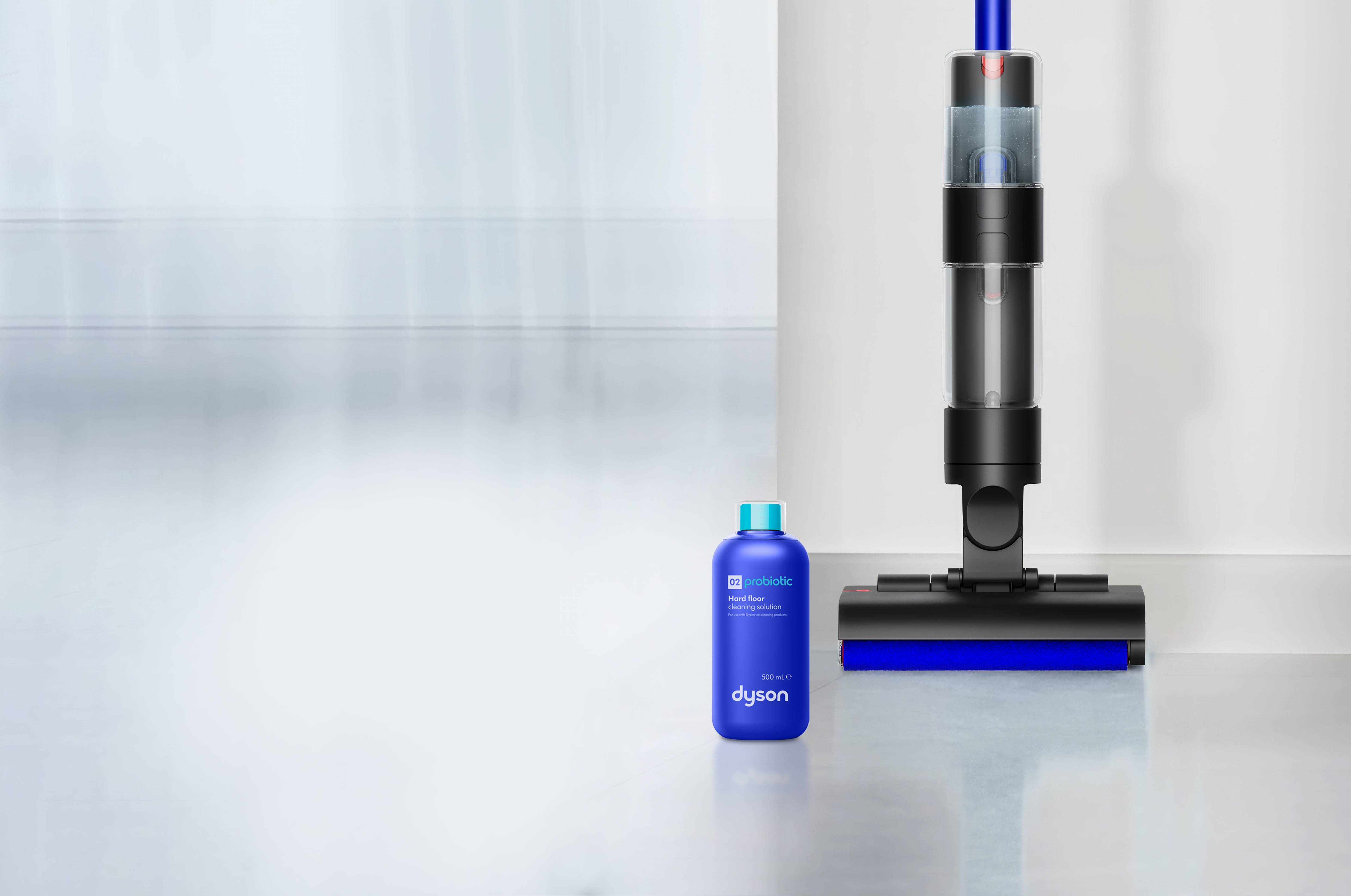 Una botella azul de solución limpiadora para suelos duros Dyson junto a una aspiradora.