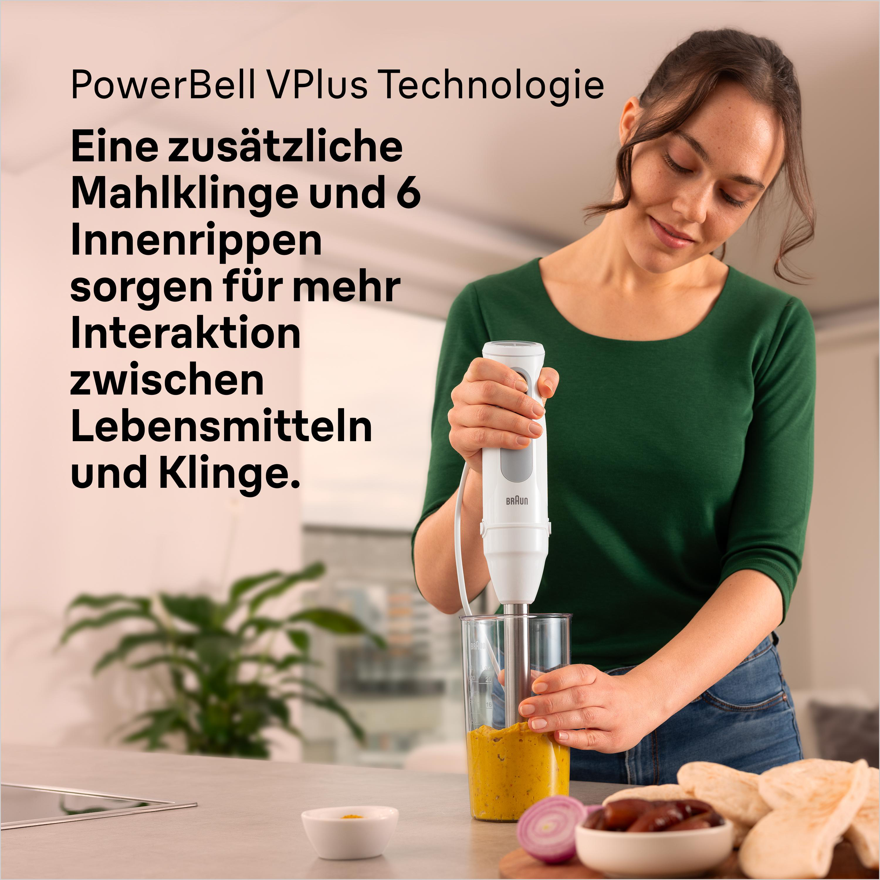 Frau mixt gelbes Püree mit einem Stabmixer im Glas. Zutaten liegen auf dem Tisch.