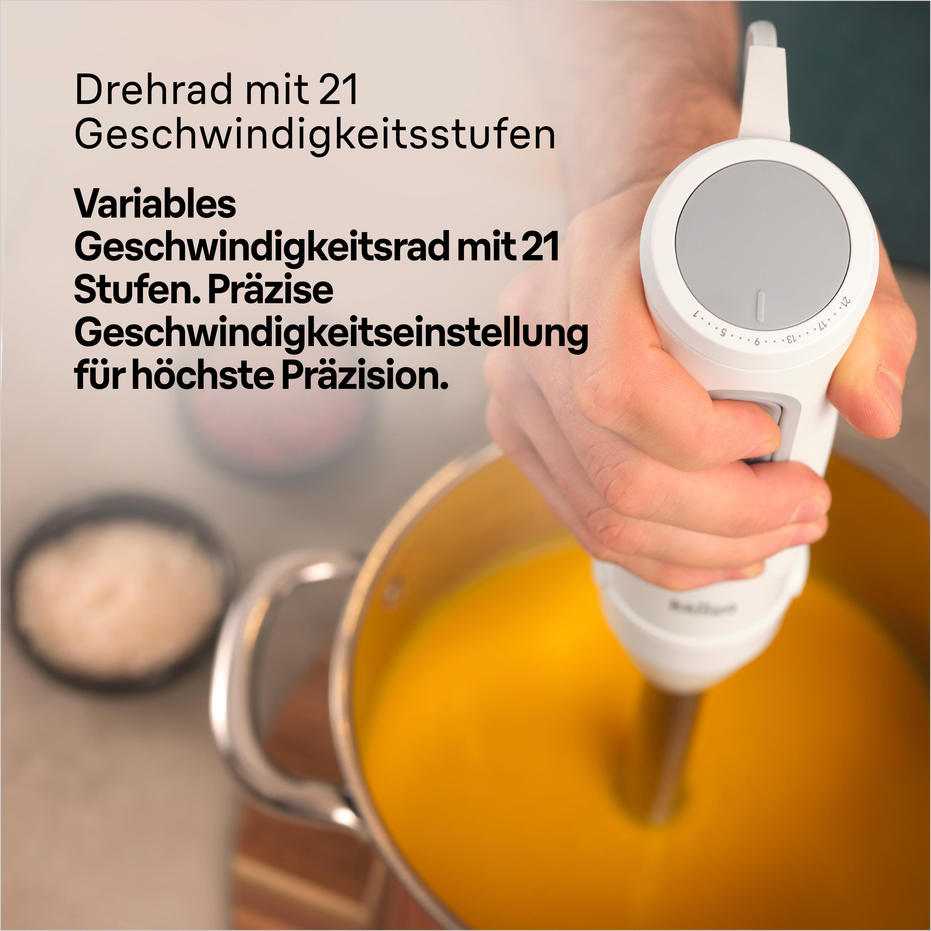 Hand hält einen weißen Stabmixer in einem Topf mit orangener Suppe, Geschwindigkeitseinstellungen sichtbar.