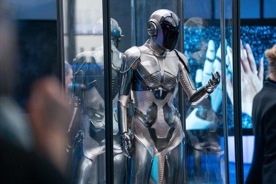 Ein silberner humanoider Roboter mit schwarzer Visier steht in einer Glasvitrine.