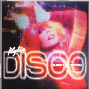 Kylie Minogue vörös hajjal és világító 'Disco' felirattal, elmosódott háttér előtt.