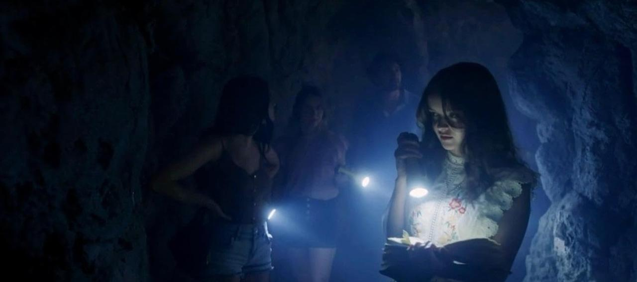 Vier Personen mit Taschenlampen in einer dunklen, felsigen Höhle. Eine Person im Vordergrund hält eine Taschenlampe.
