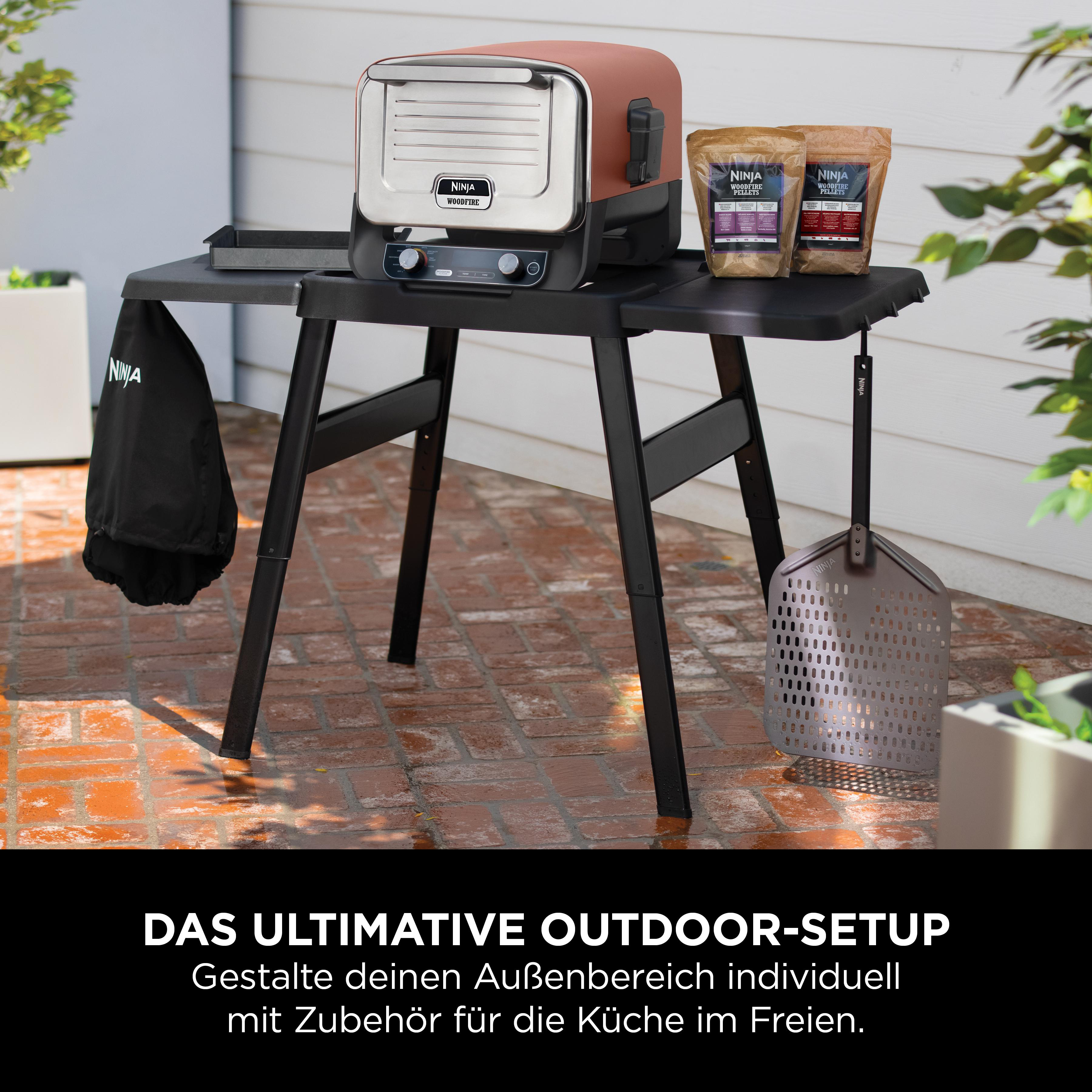 Ein Ninja Woodfire Grill mit Zubehör steht auf einem Tisch im Freien.