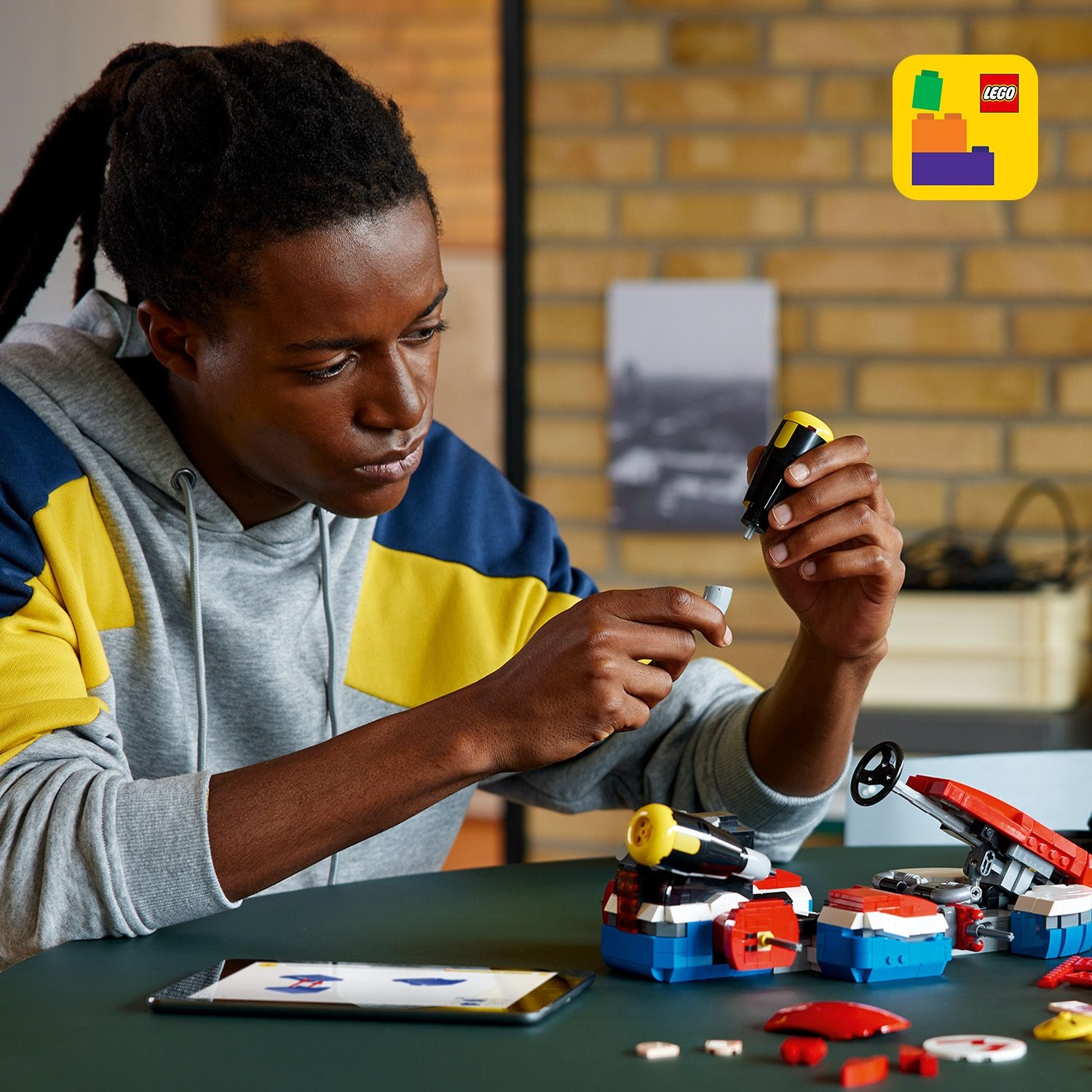 Un giovane con dreadlocks costruisce un'auto Lego rossa e blu, tenendo un piccolo pezzo giallo e nero.
