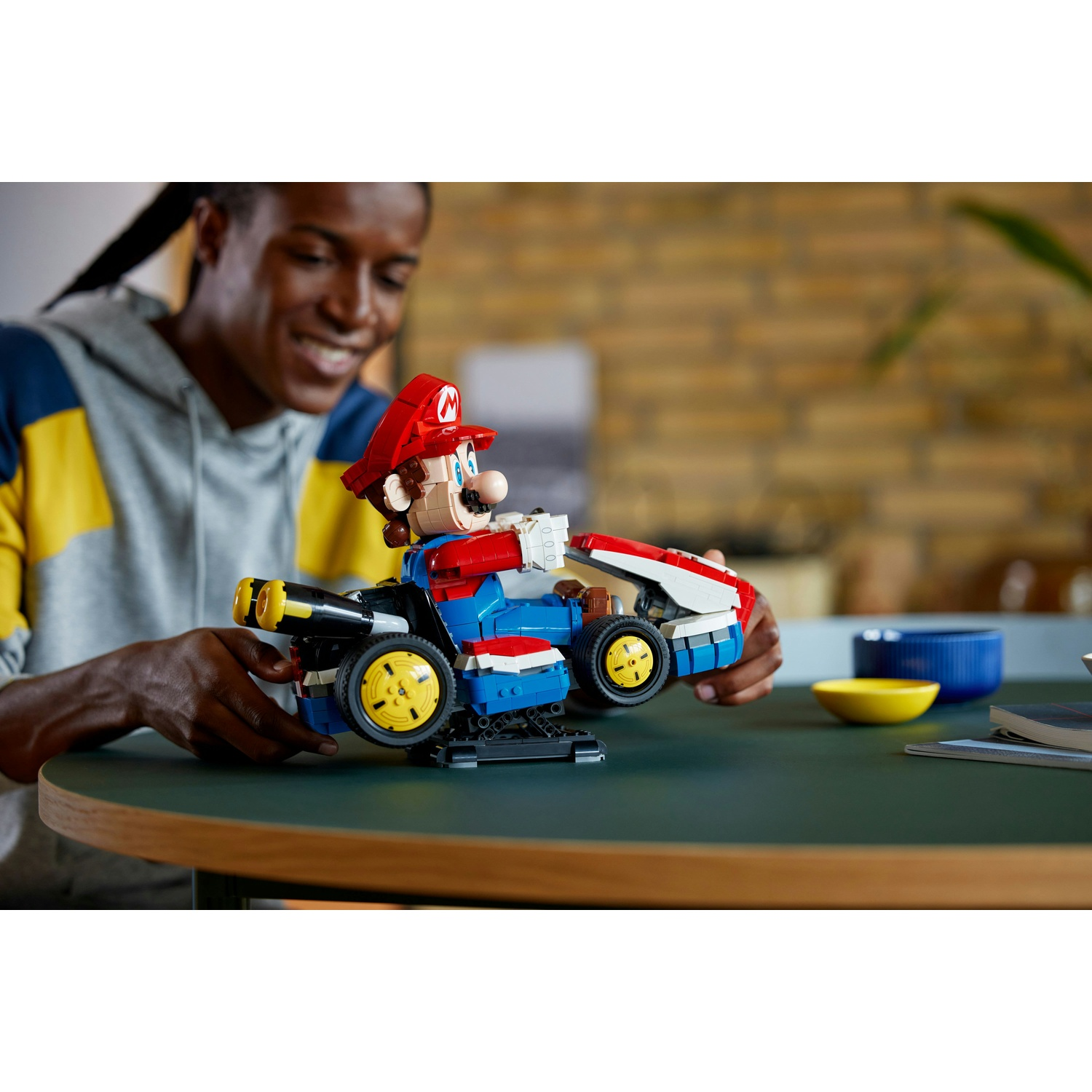 Uomo costruisce LEGO Mario Kart con veicolo blu, rosso e bianco su tavolo verde.