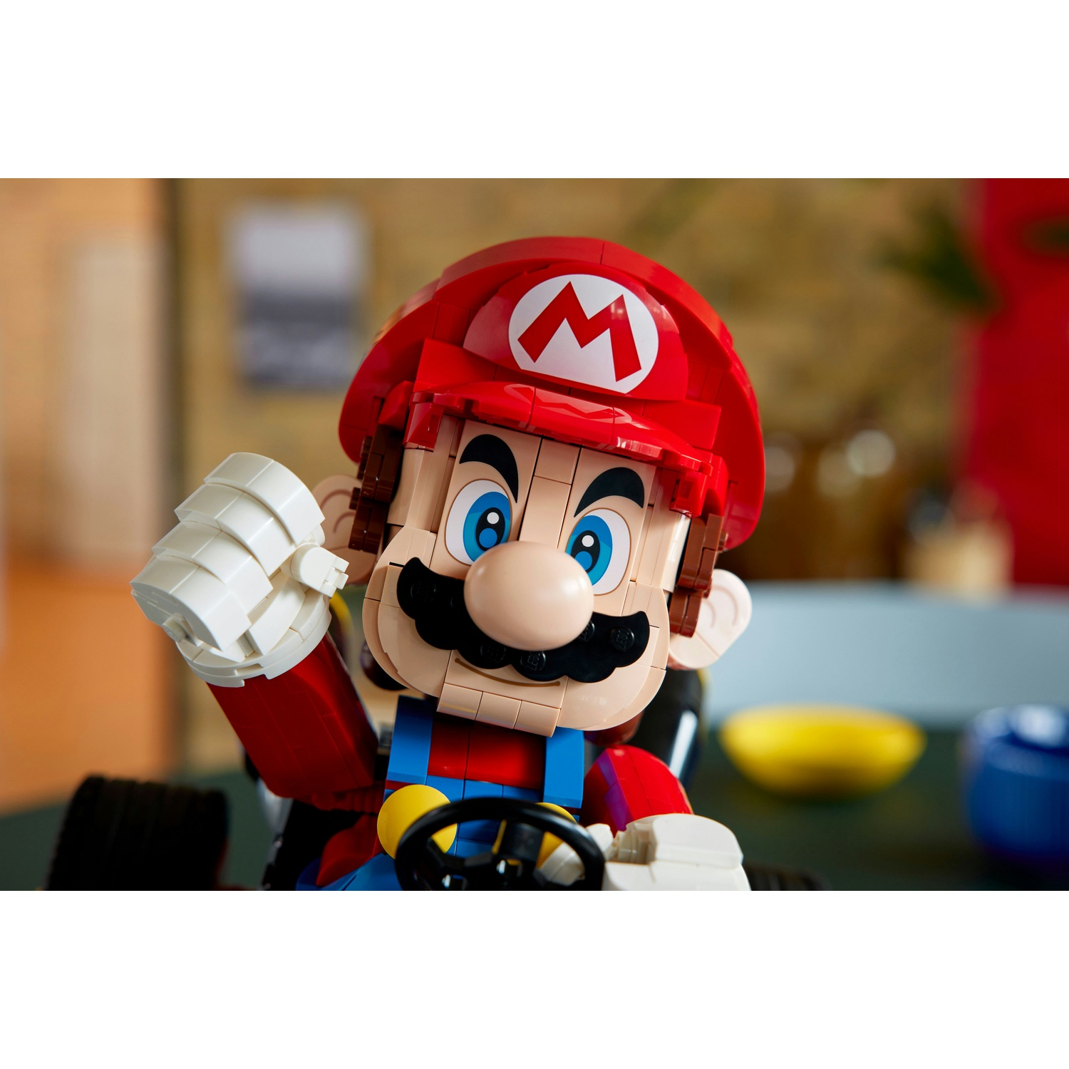 Lego Mario con cappello rosso e tuta, guida un kart, con banana gialla e tazza blu sullo sfondo.