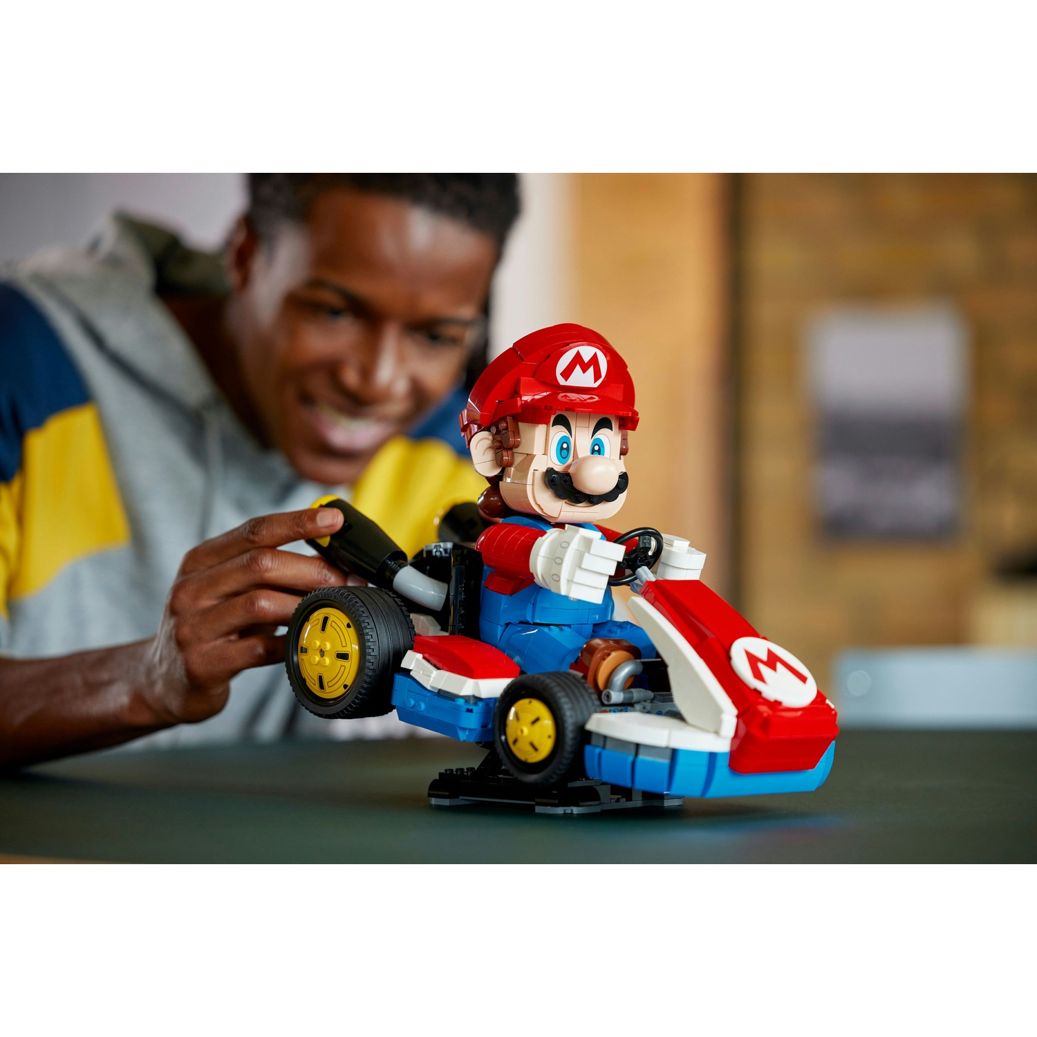 Un uomo gioca con un giocattolo Lego Mario Kart. Mario è rosso, blu e bianco con ruote gialle.