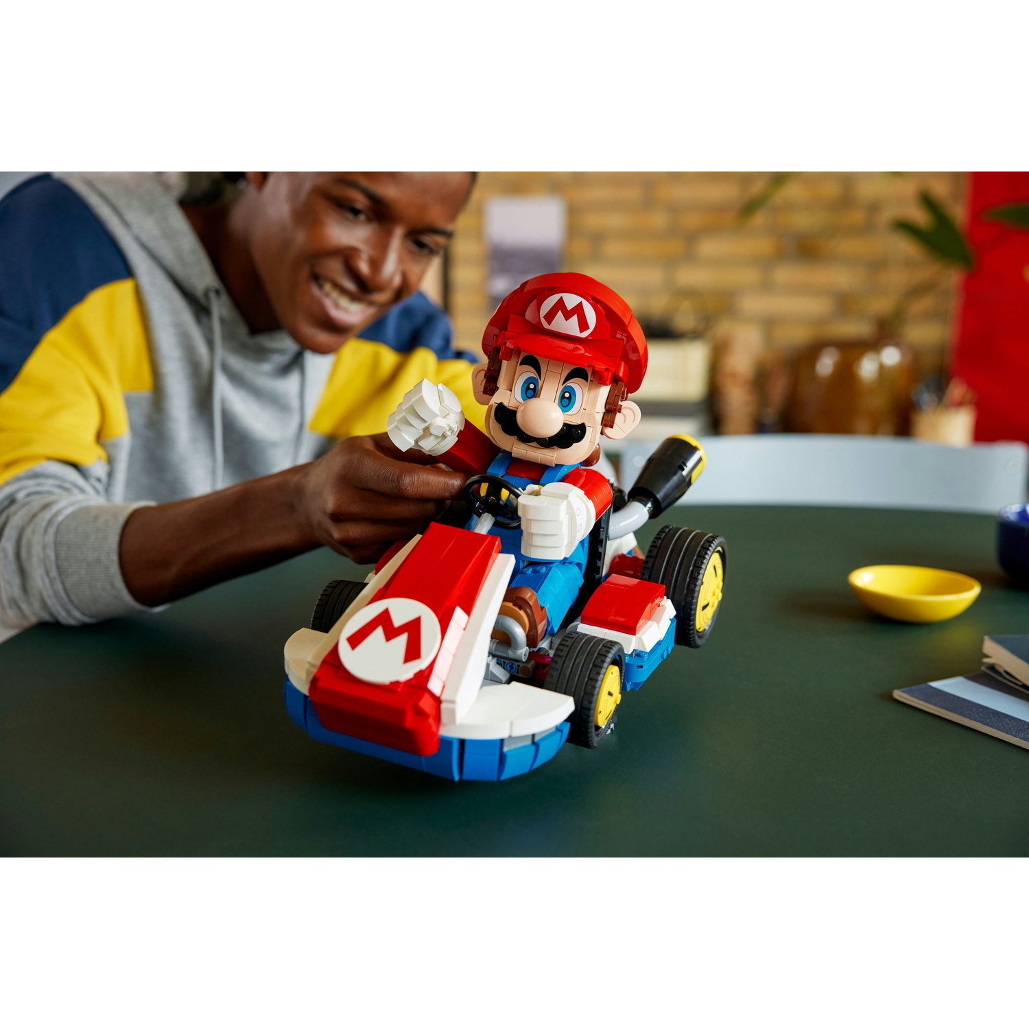 Uomo costruisce Lego Mario Kart con parti rosse e blu.