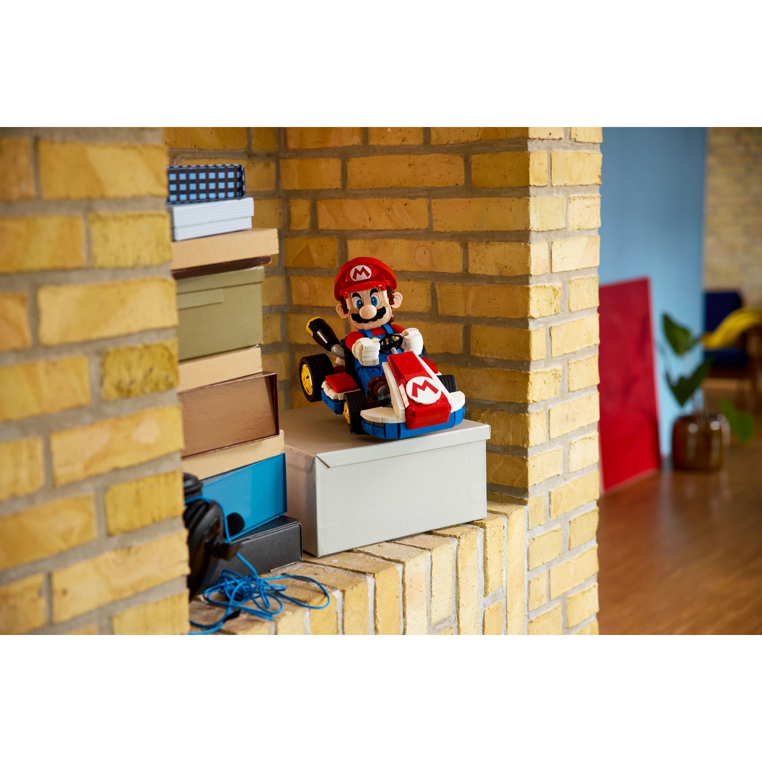 Mario in un Go-Kart siede su una scatola grigia contro un muro di mattoni.