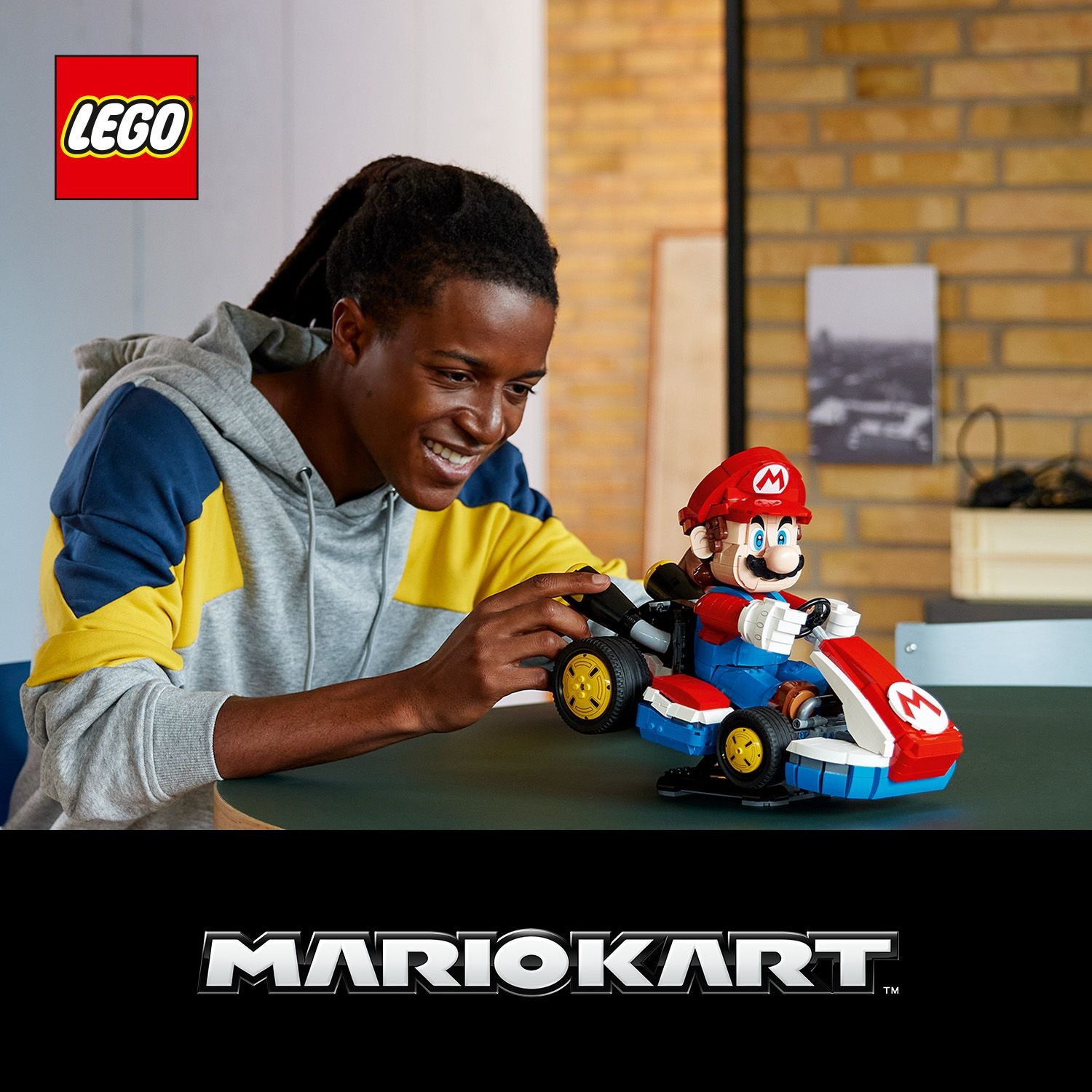 Un giovane sorride mentre assembla un veicolo LEGO Mario Kart. Il logo LEGO è visibile.