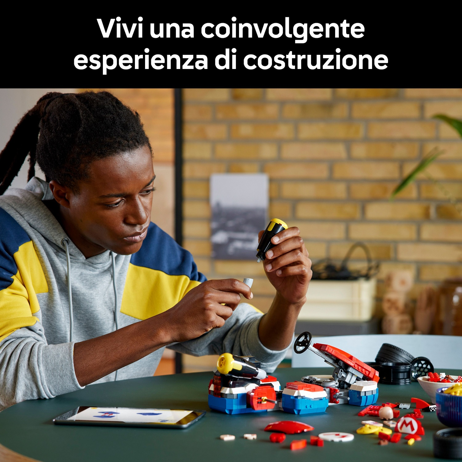 Una persona nera giovane costruisce con mattoncini LEGO colorati, un tablet mostra le istruzioni.