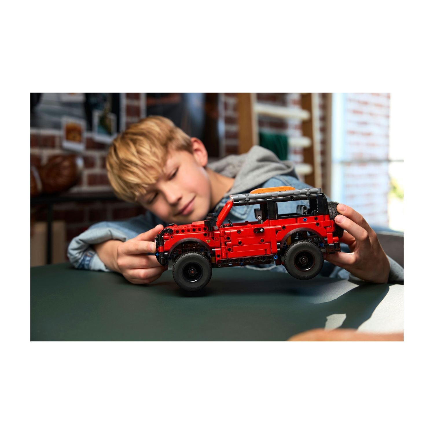 Un ragazzo tiene un'auto Lego rossa. Indossa una giacca di jeans e una felpa grigia.