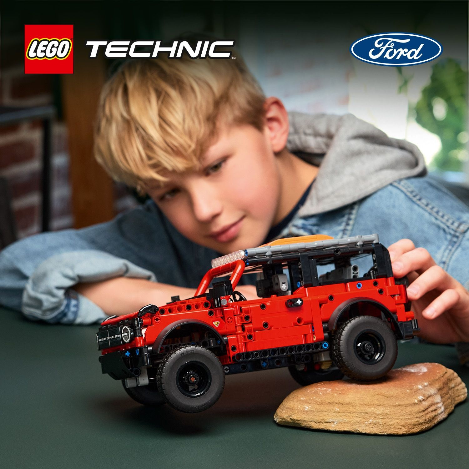 Un ragazzo costruisce un Ford Bronco rosso Lego Technic su un tavolo. Il logo Ford è visibile.