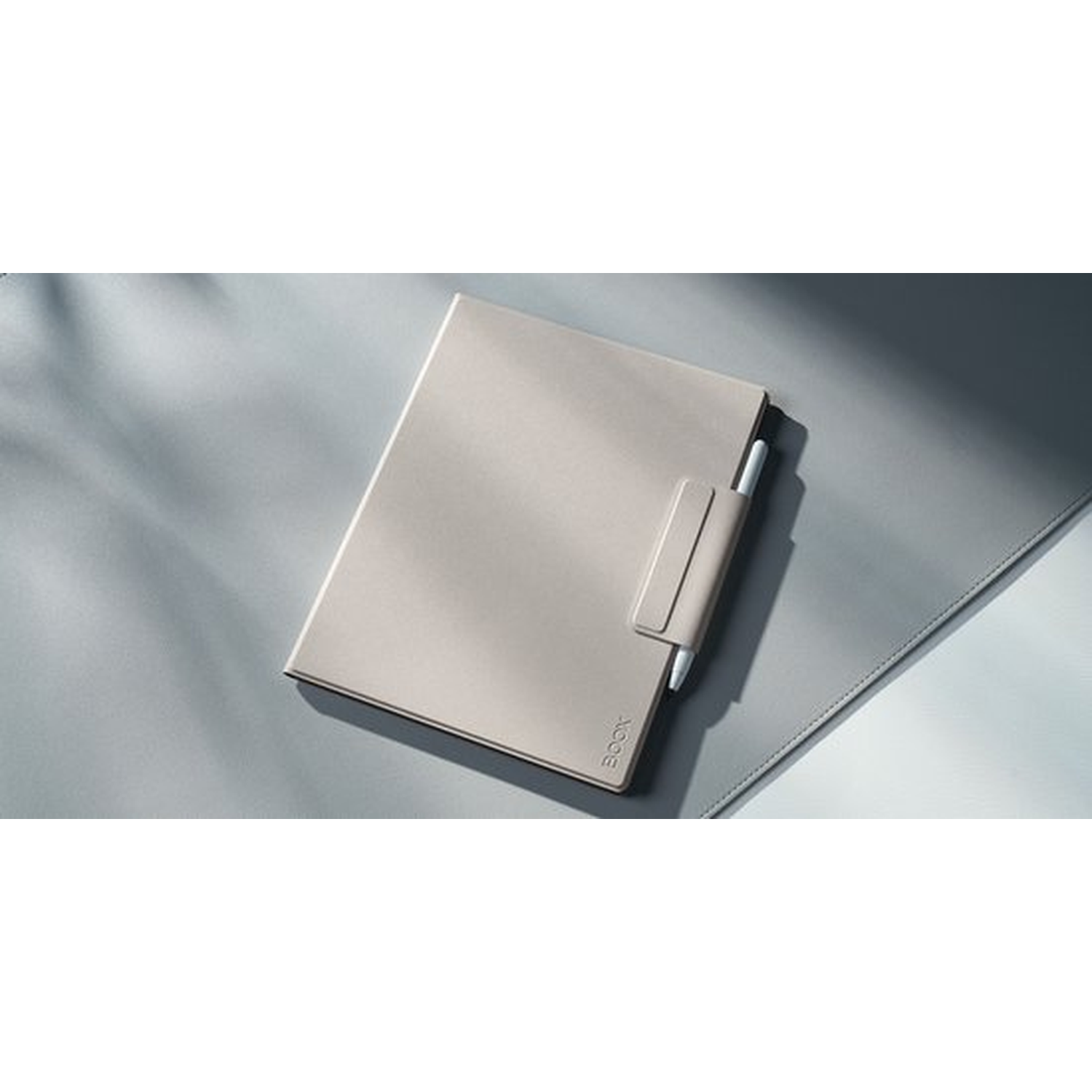 Een lichtbeige e-reader met een stylus in een houder, op een grijze ondergrond.