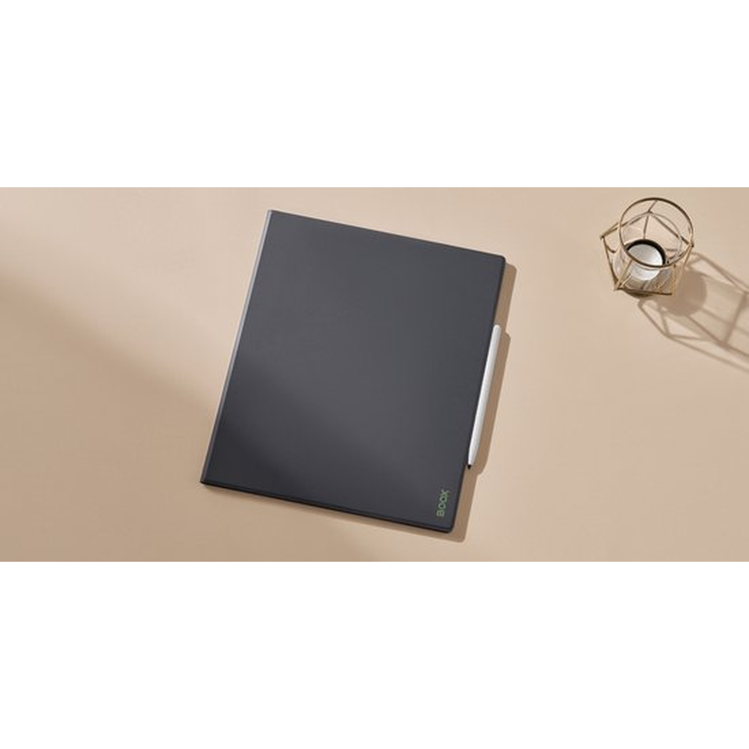 Een donkergrijs tablet met stylus rust op een beige oppervlak. Een decoratieve gouden kandelaar staat in de buurt.