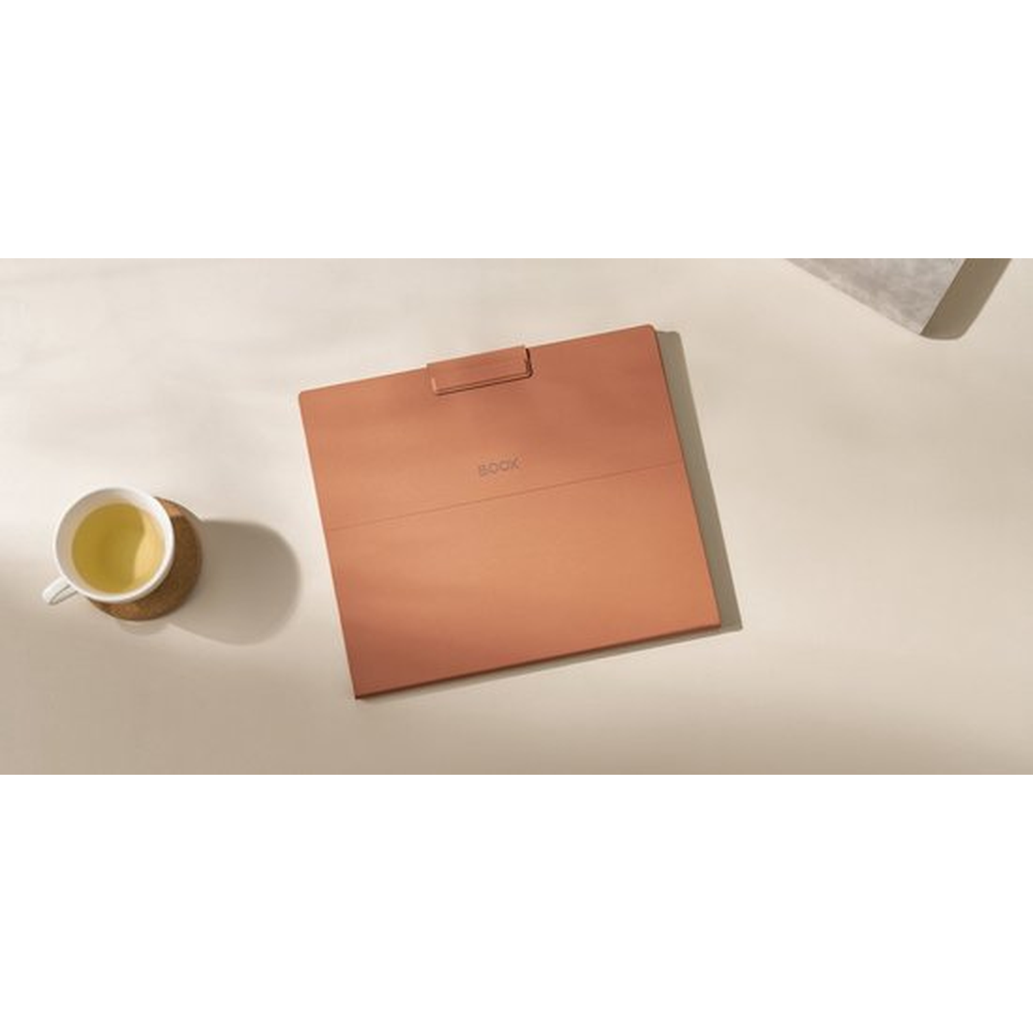 Een koperkleurig tablet ligt op een beige ondergrond naast een kop thee.