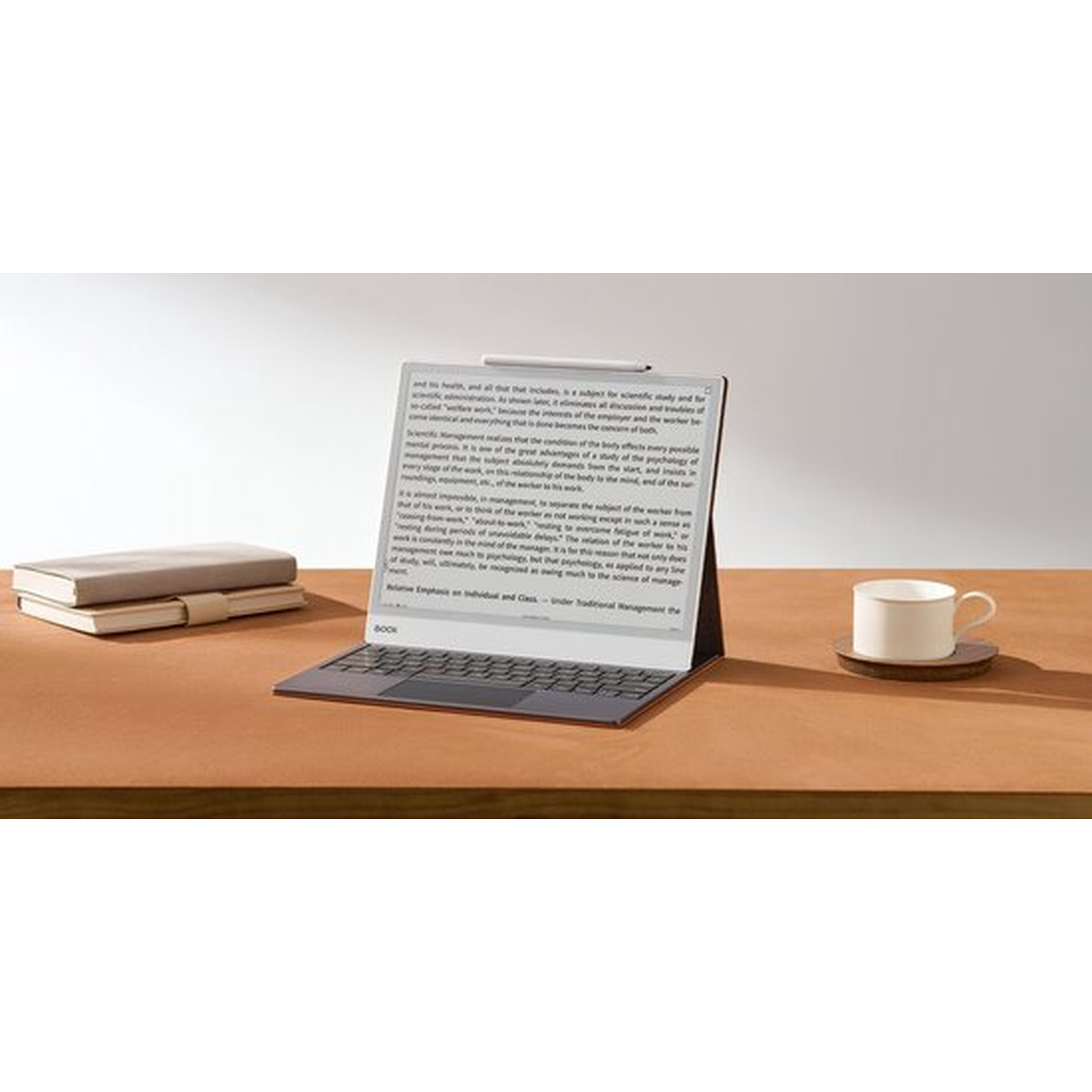 Een digitale tablet met toetsenbord, twee boeken en een kop thee op een houten bureau.