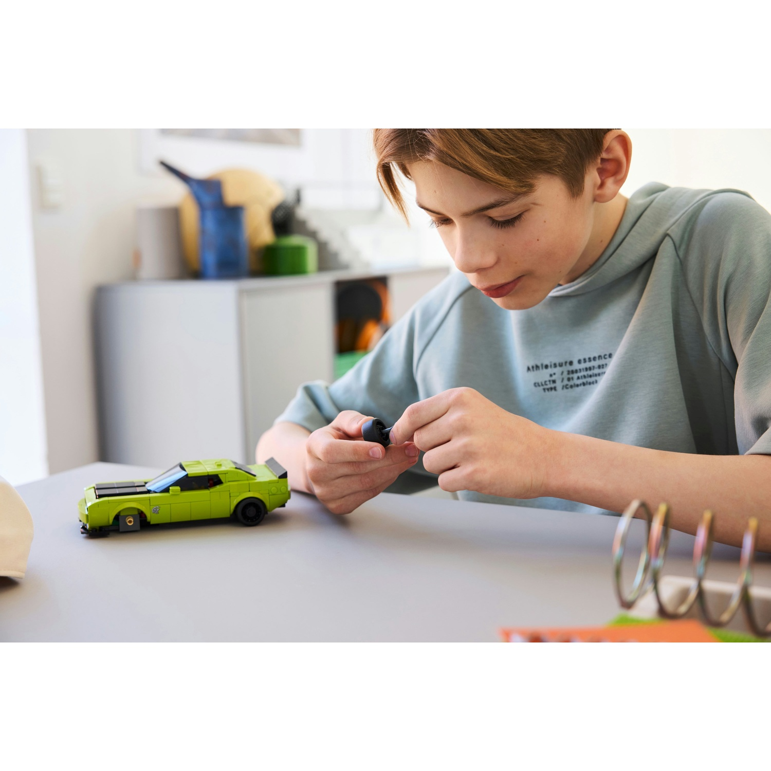 Un ragazzo costruisce un'auto Lego verde. È concentrato nel collegare un piccolo pezzo nero.
