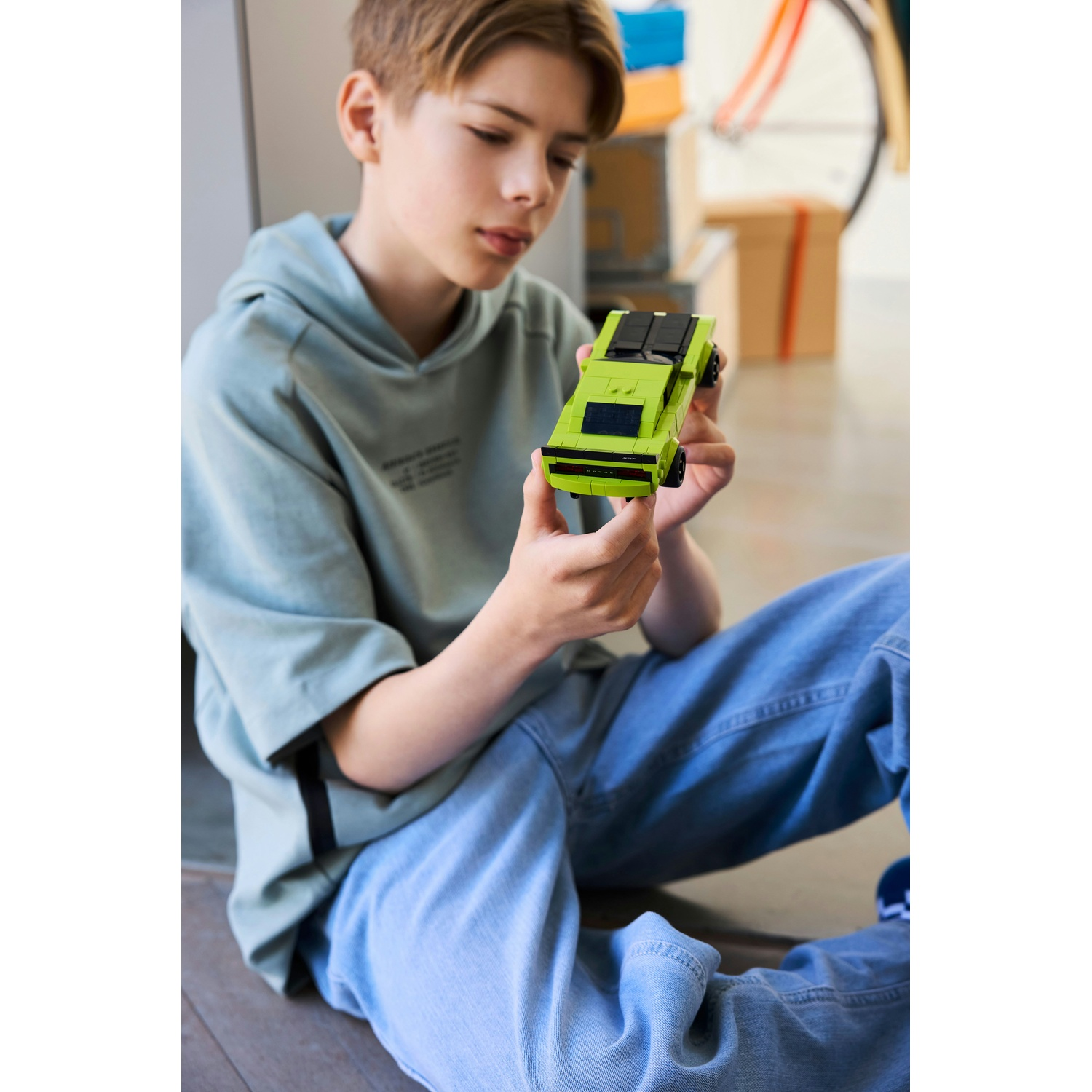 Un ragazzo in felpa azzurra e jeans tiene in mano una macchinina verde lime.
