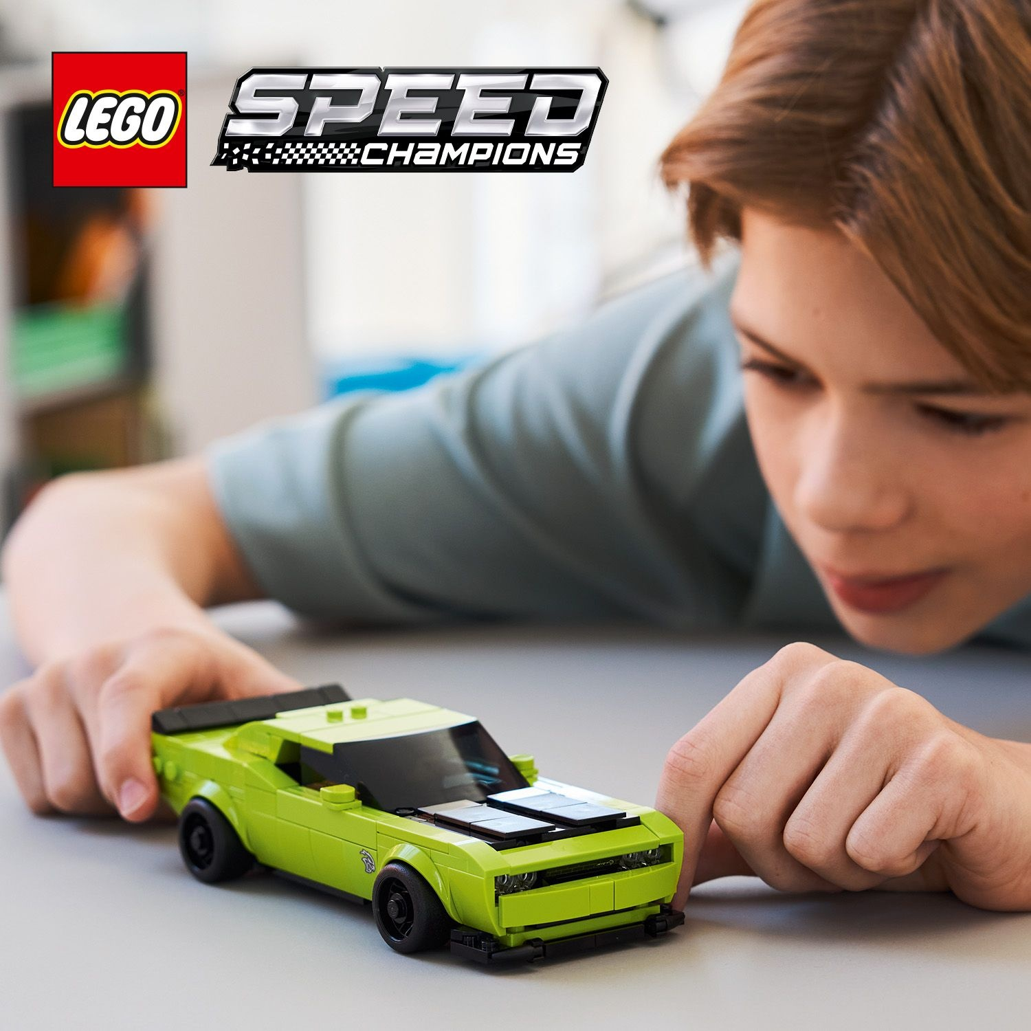 Ragazzo gioca con una macchinina Lego verde. Logo Lego Speed Champions visibile.