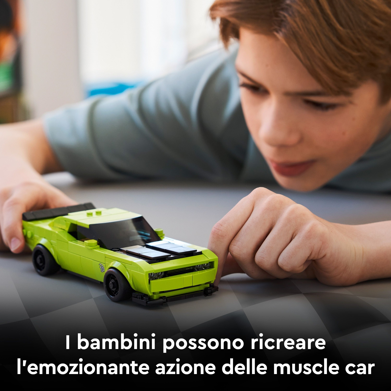 Un bambino gioca con un'auto muscolosa LEGO verde su una superficie a scacchi.