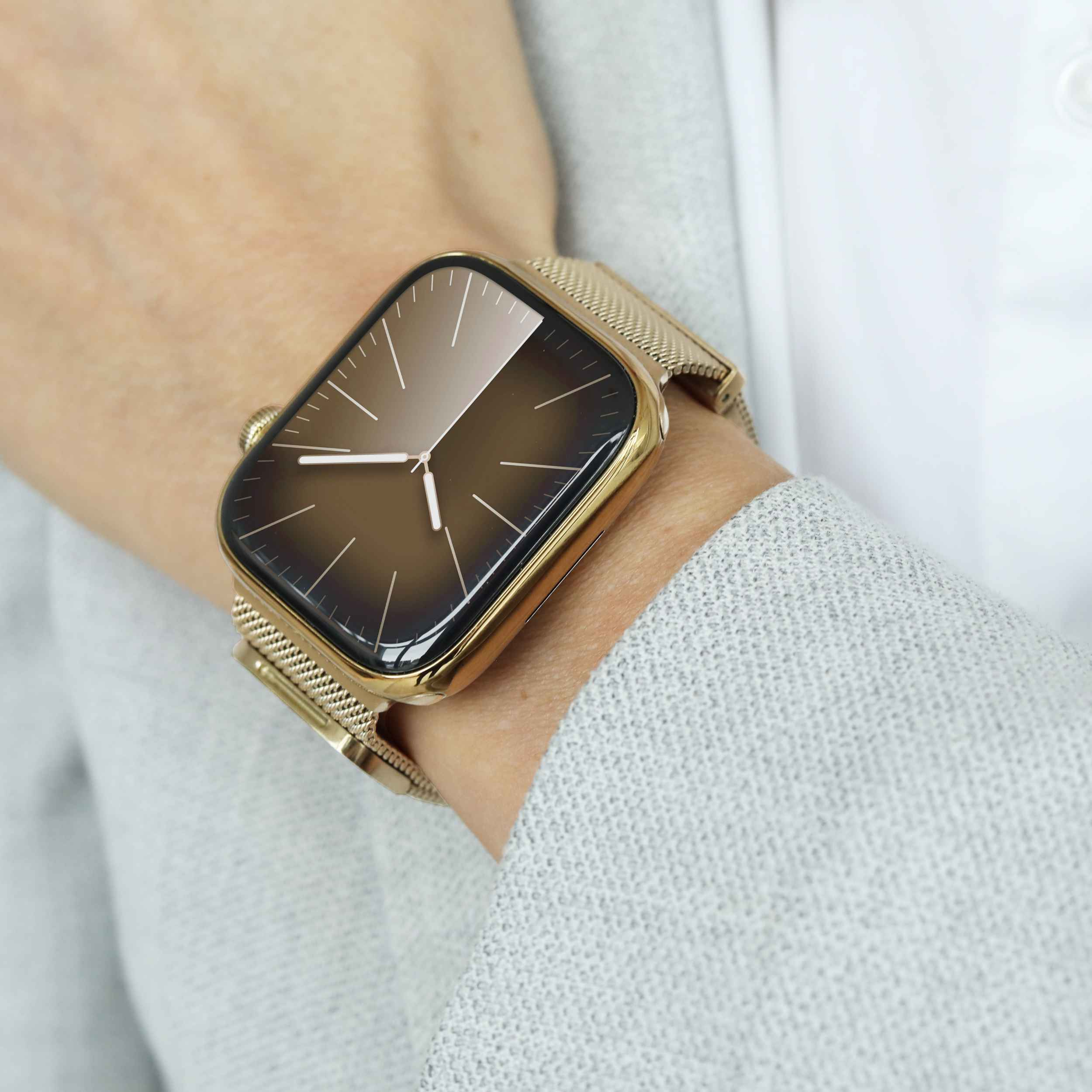 Une montre connectée dorée avec bracelet en maille au poignet, affichant un cadran analogique marron.