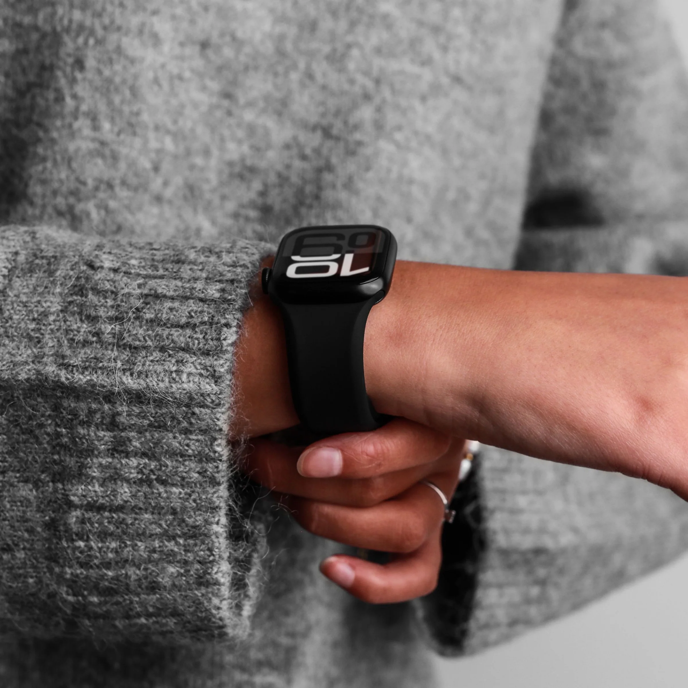 Eine Person trägt einen grauen Strickpullover und eine schwarze Smartwatch mit der Anzeige 10:09.