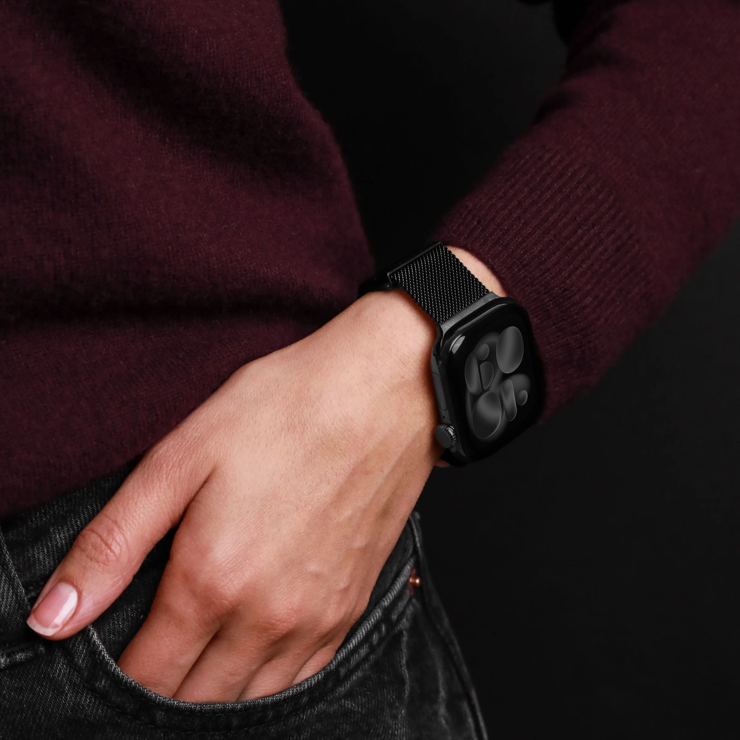Une personne portant un pull bordeaux et une montre connectée noire à bracelet milanais.