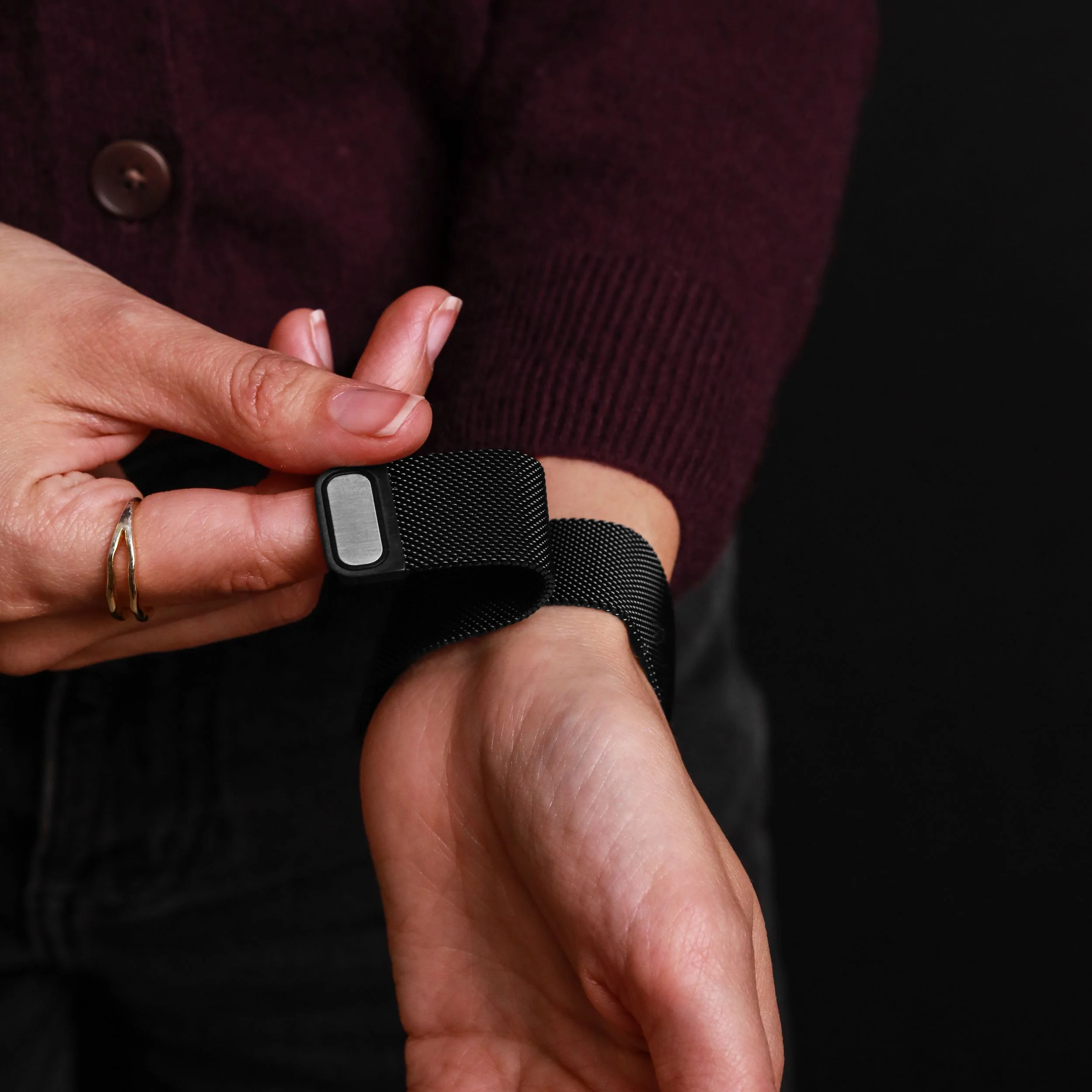 Personne attachant un bracelet Milanais noir à un poignet.