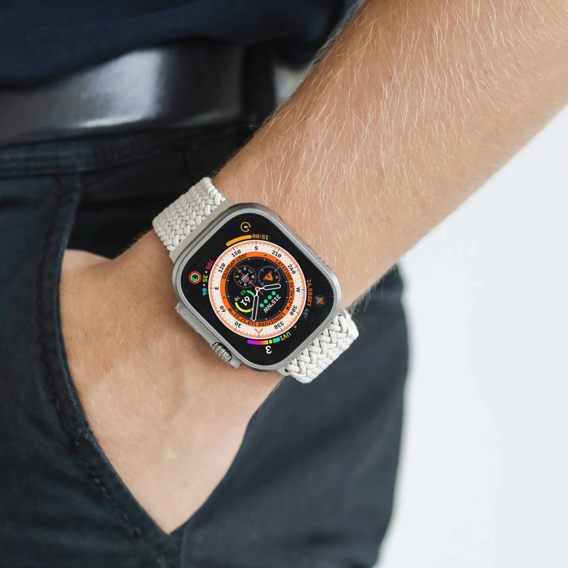 Primo piano del polso di una persona con uno smartwatch argentato con cinturino intrecciato bianco. Il quadrante mostra ora e bussola.