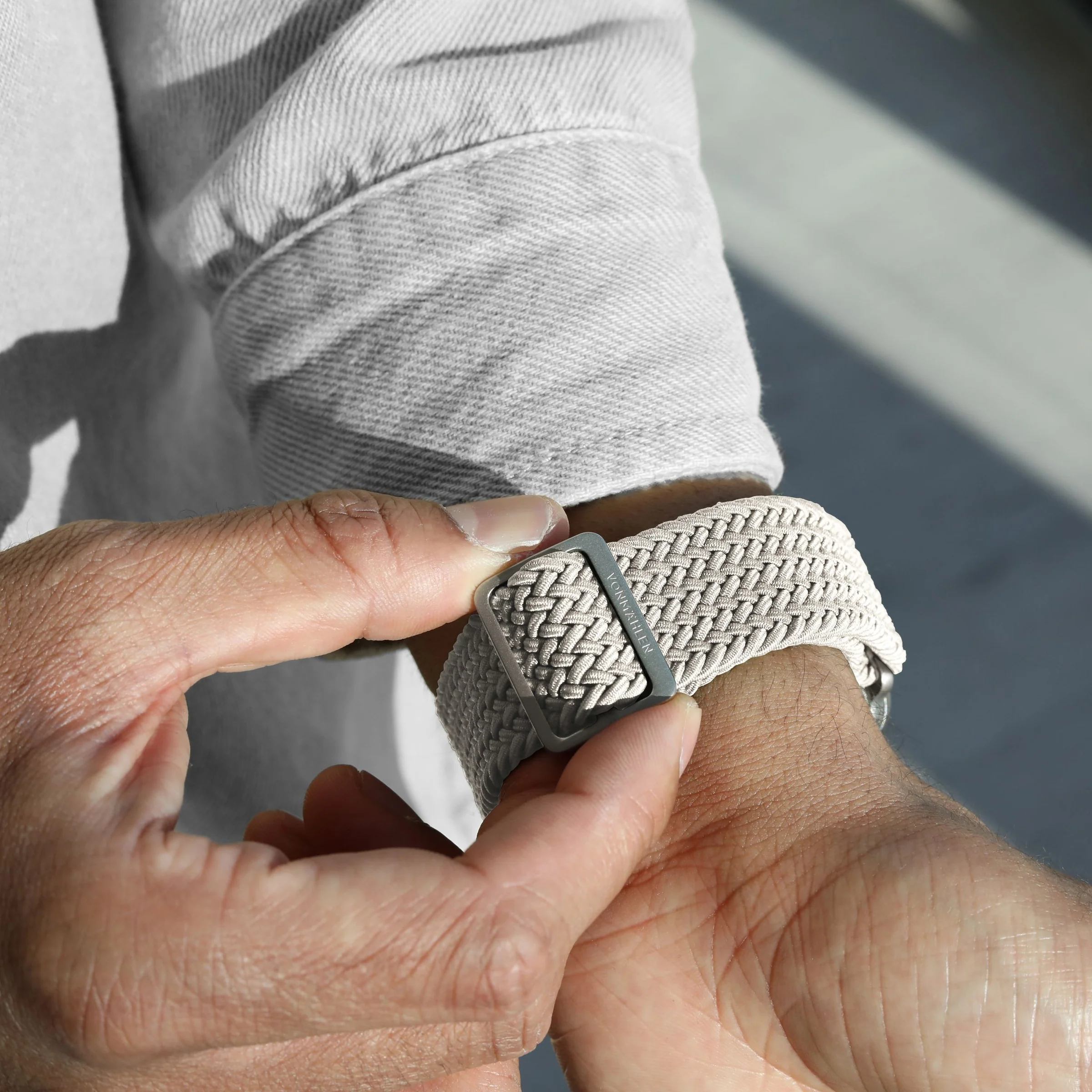 Una persona allaccia un cinturino d'orologio in tessuto grigio con fibbia in metallo.