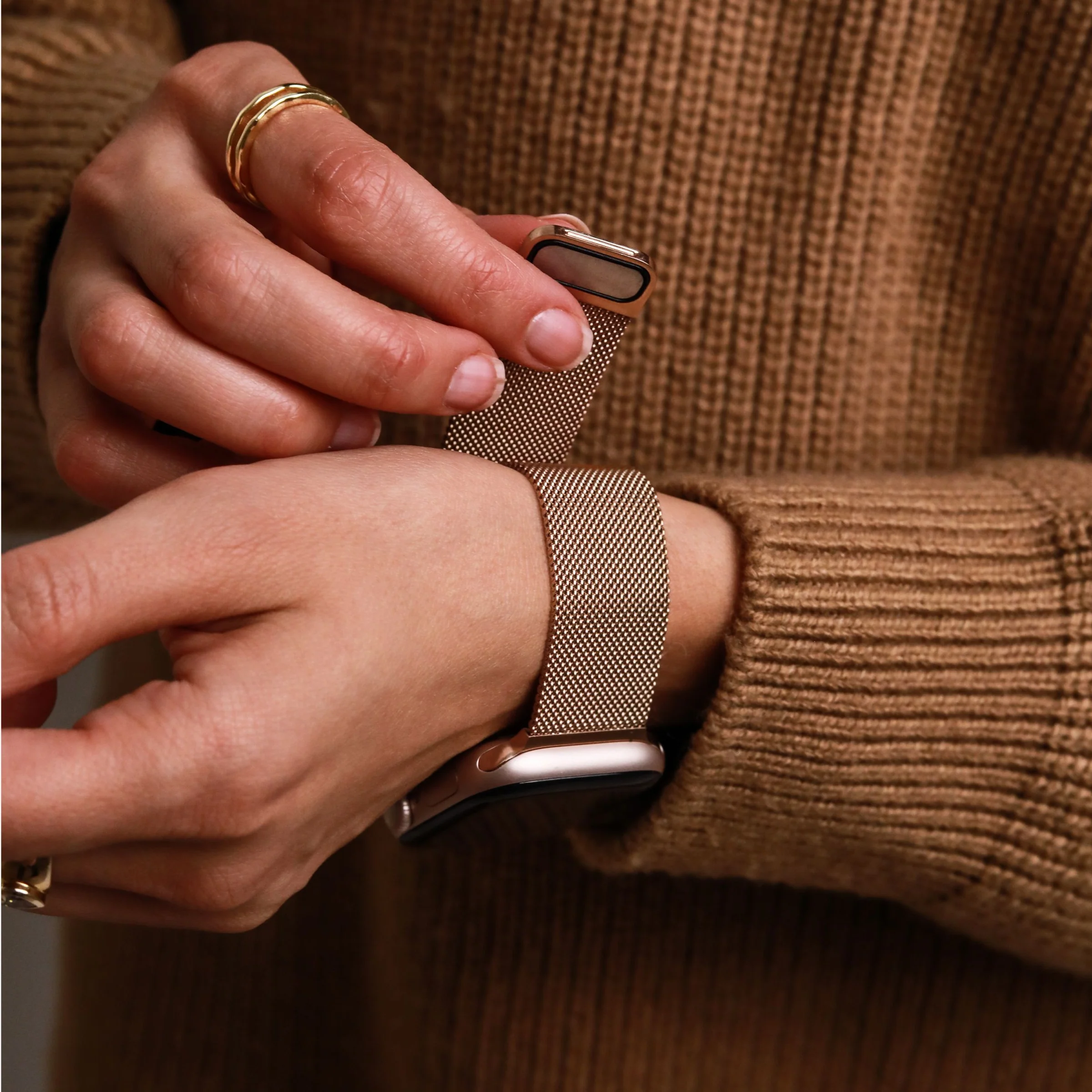 Une personne avec des bagues dorées à la main attache un bracelet de montre connectée.