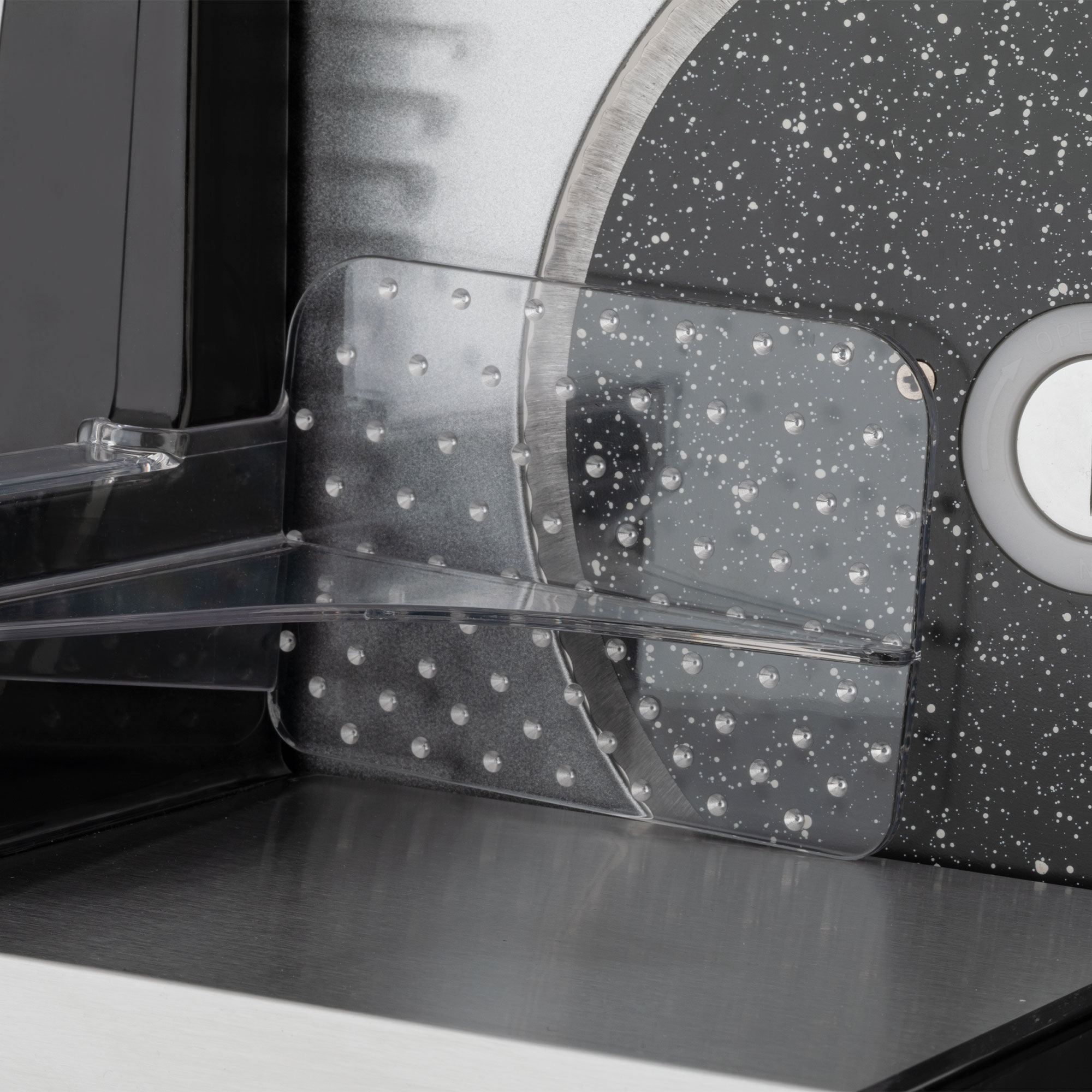 Primer plano de una cuchilla de cortadora con protector de plástico transparente y superficie moteada.