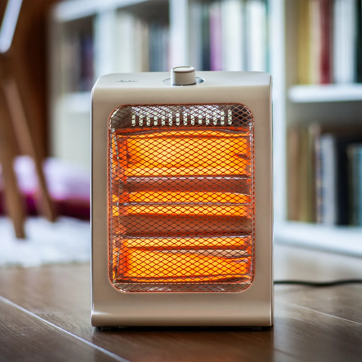 Un calentador eléctrico portátil con elementos calefactores naranjas brillantes está sobre un suelo de madera.