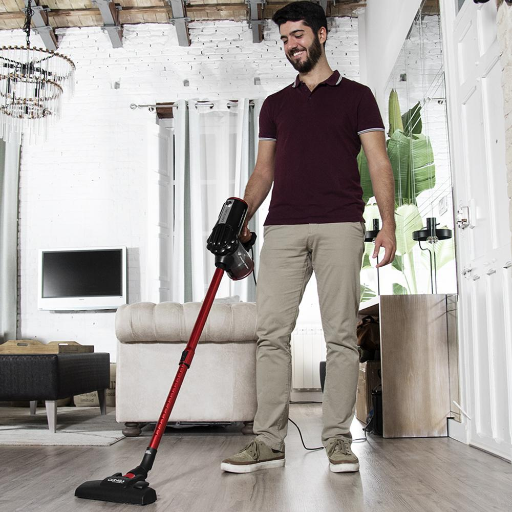 Un hombre aspira un suelo de madera con una aspiradora roja.
