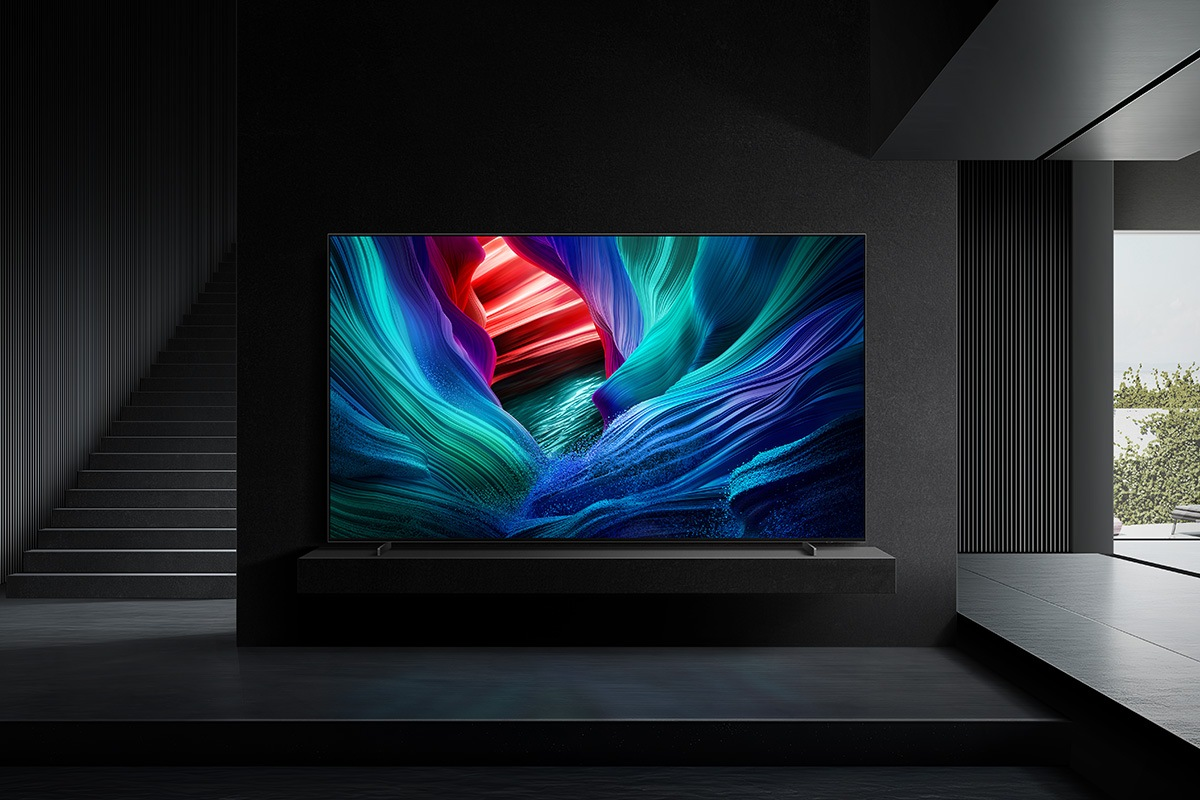 Une grande télévision affiche des vagues abstraites et colorées dans une pièce sombre et moderne avec des escaliers.