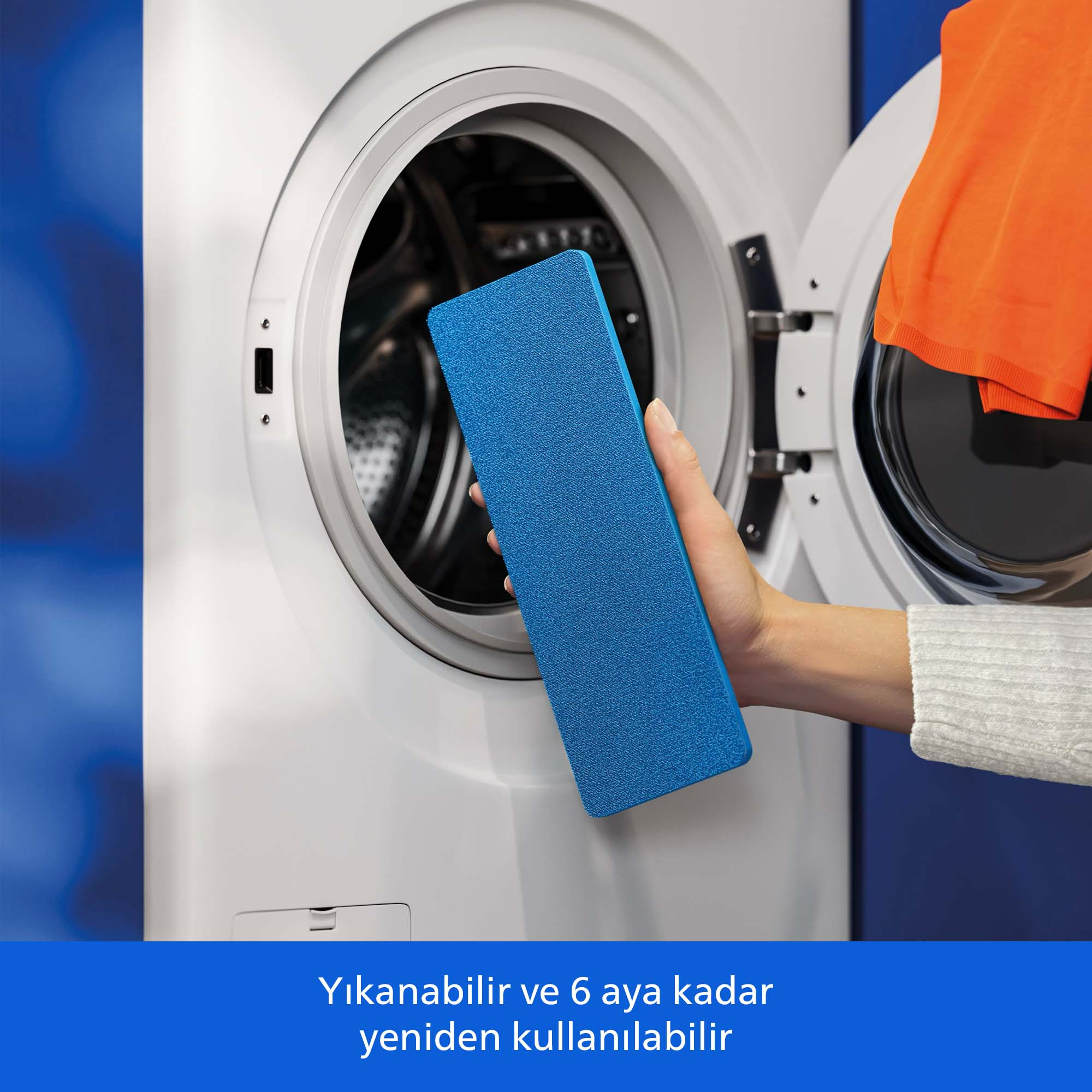Bir el, turuncu giysili çamaşır makinesinin önünde mavi sünger tutuyor.