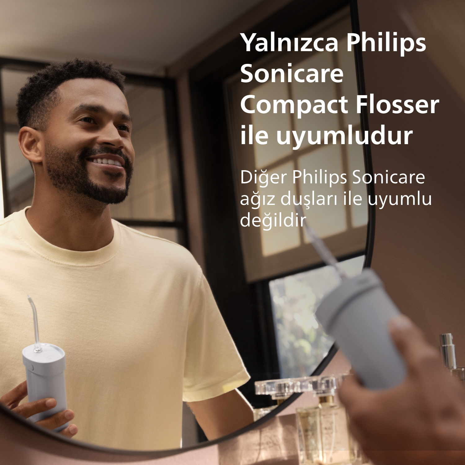 Bir adam ayna yakınında Philips Sonicare Compact Flosser tutuyor.