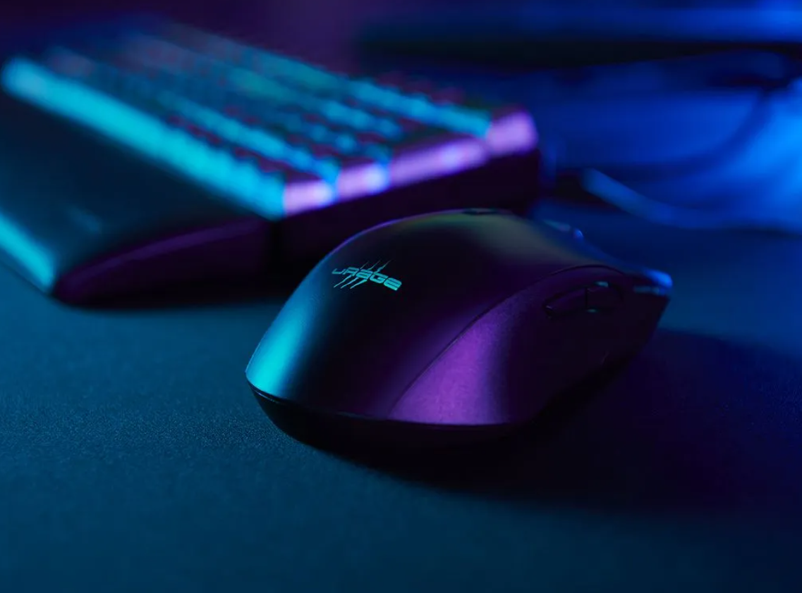 Eine schwarze Maus mit blauem Logo vor einer unscharfen Tastatur im Dunkeln.