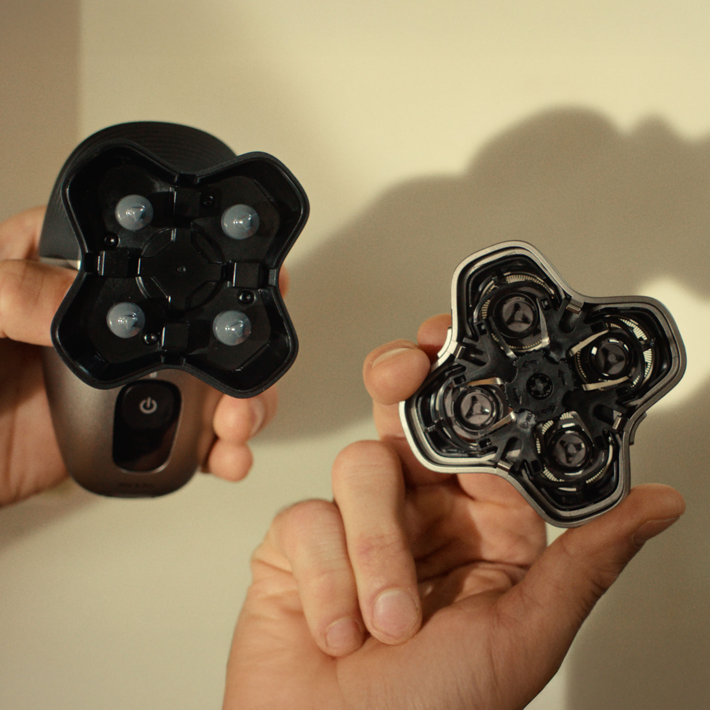 Dwie ręce trzymają golarkę elektryczną i jej zdejmowaną głowicę z ostrzami.