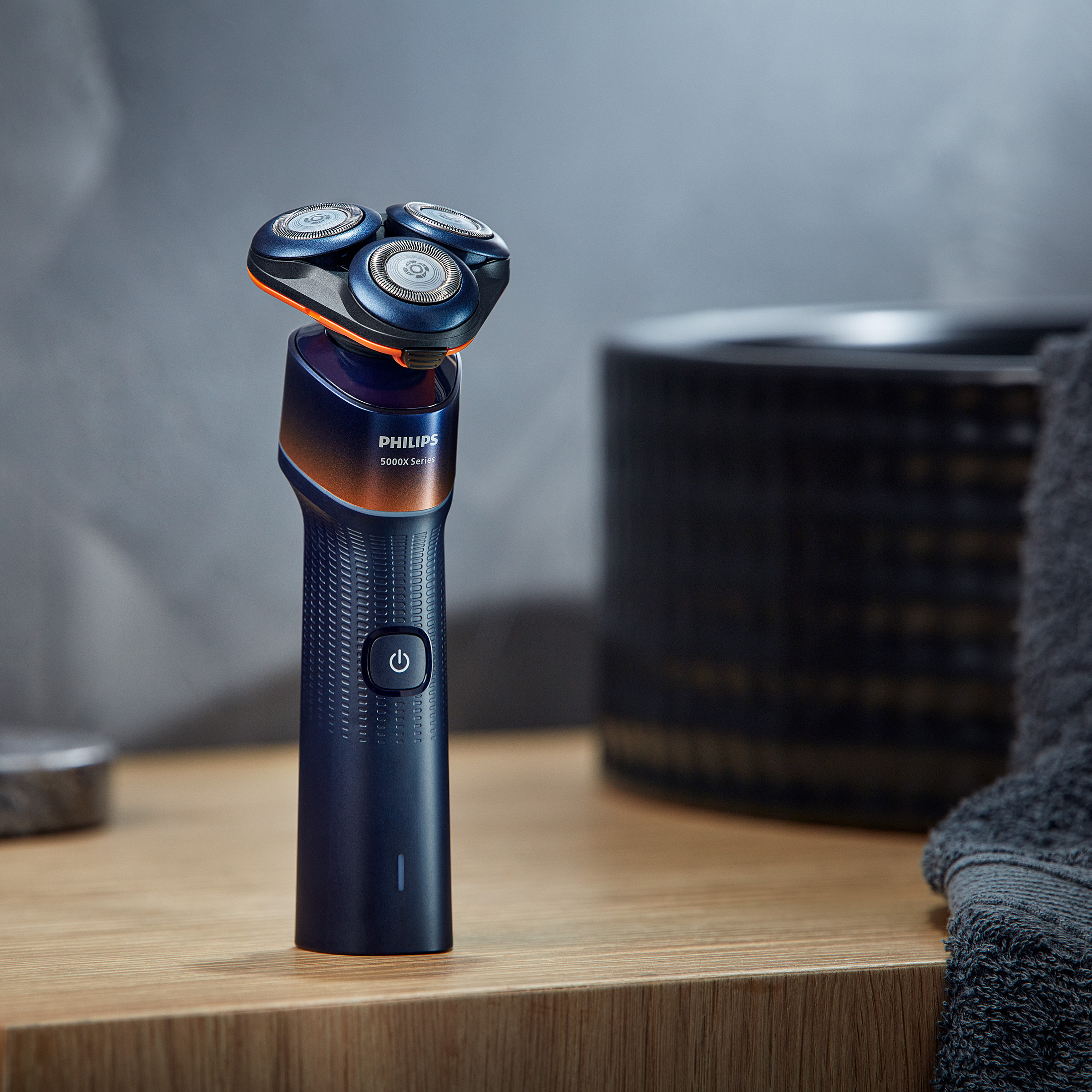 Niebieska maszynka do golenia Philips z obrotową głowicą spoczywa na drewnianej półce.