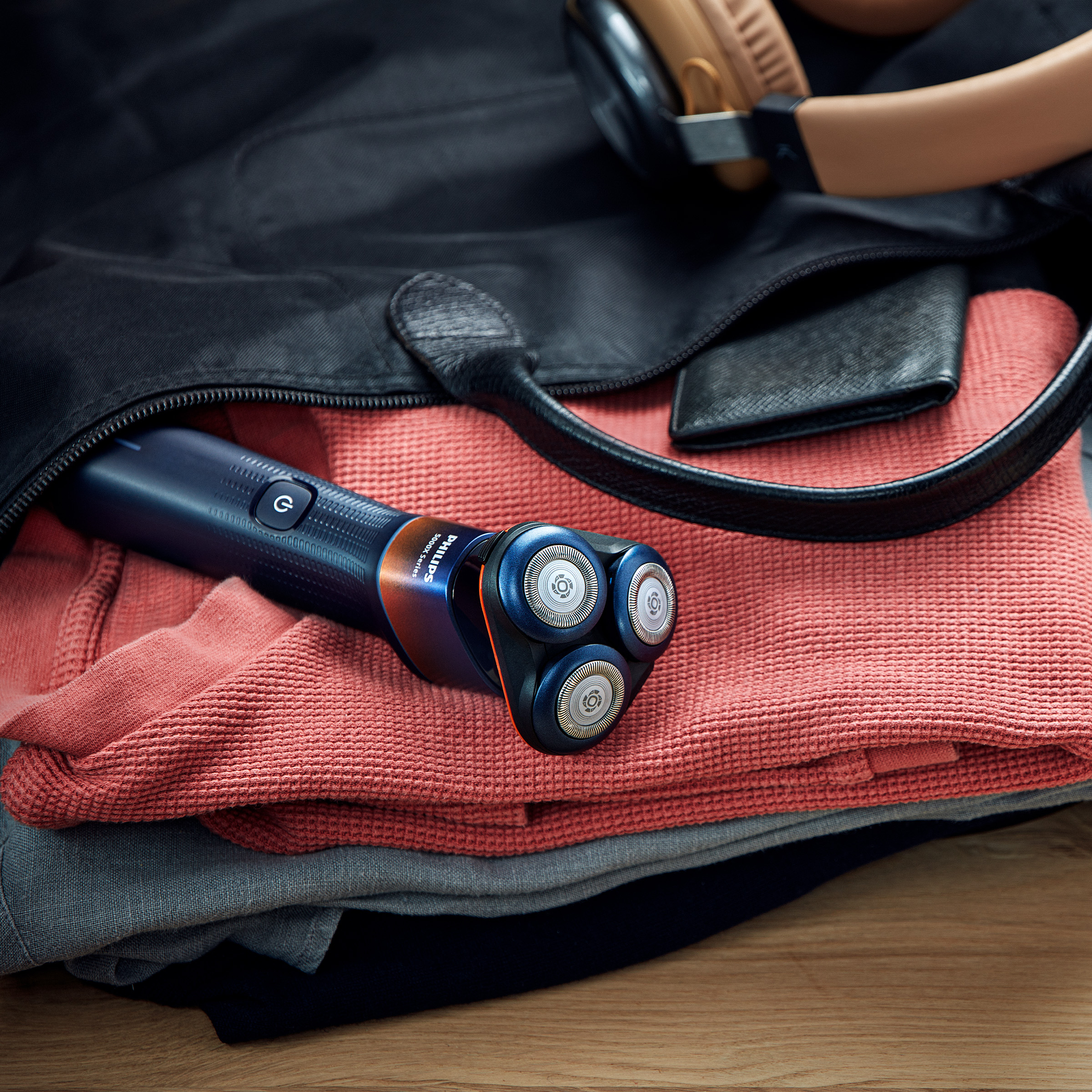 Golarka leży na ubraniach w torbie ze słuchawkami i portfelem.